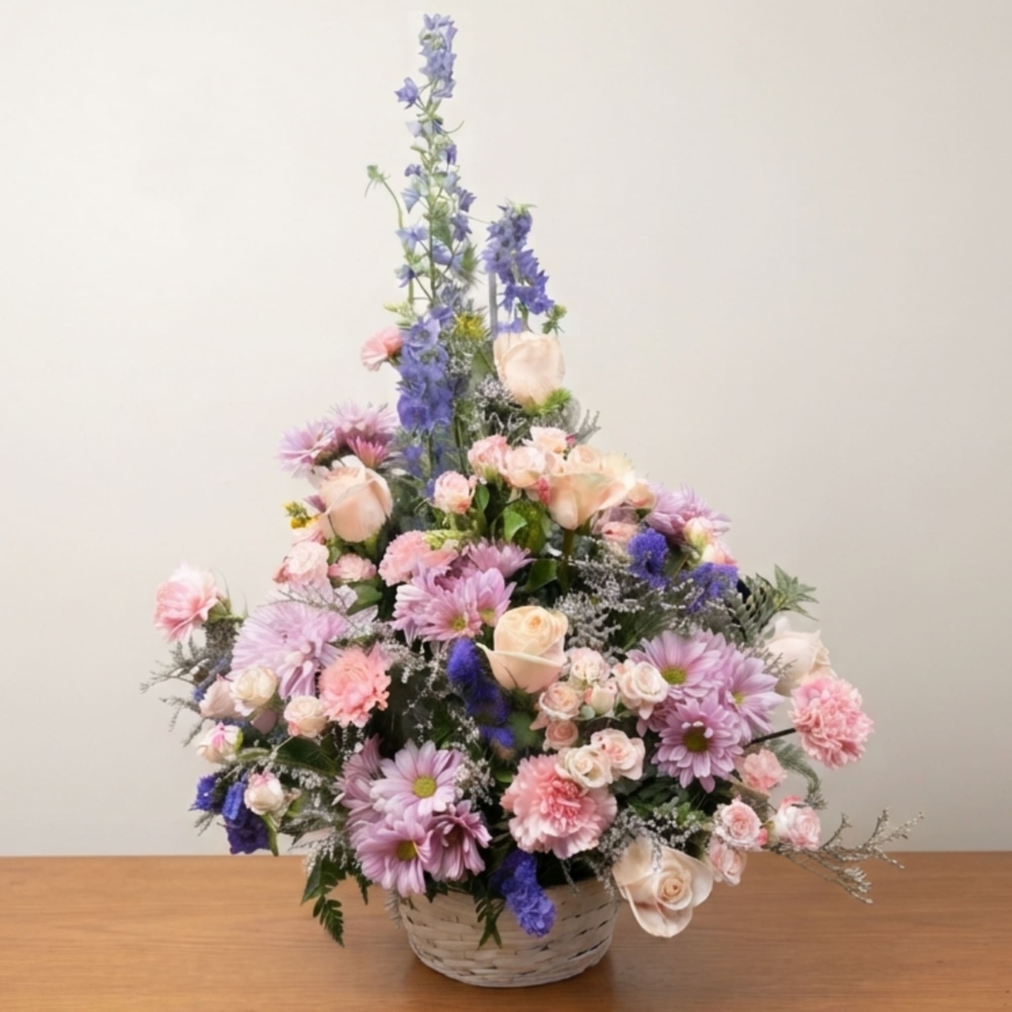 Pastel floral arrangement in a woven basket with tall blue blooms and pink flowers