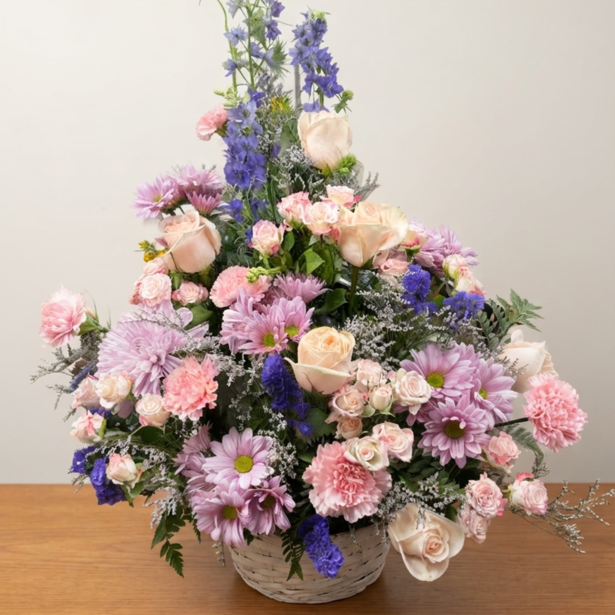 Basket arrangement of pink and lavender flowers with cream roses