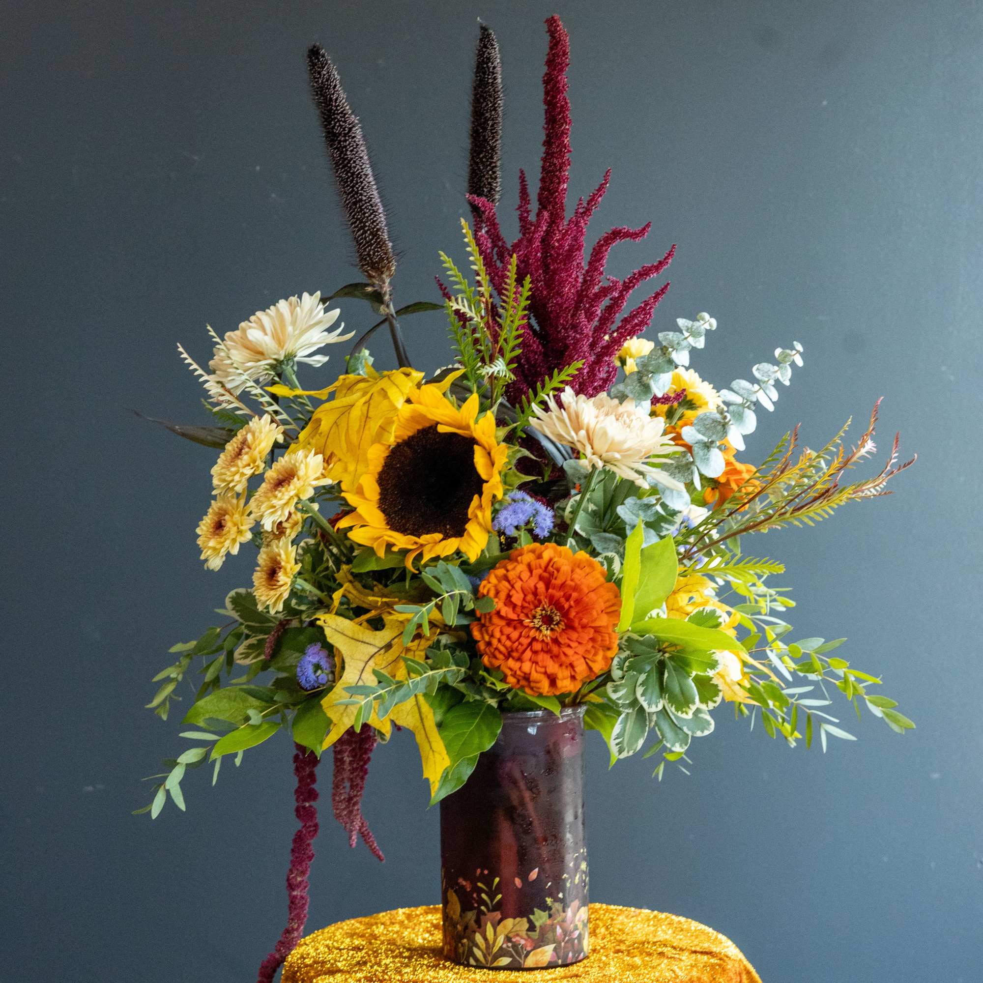 Tall mixed bouquet with sunflower, orange zinnia, and daisies in a dark vase