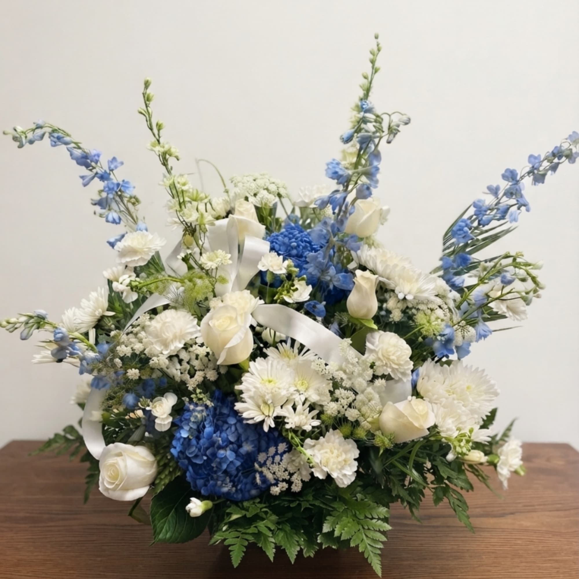 Blue and white floral arrangement with roses and ribbon in a low container