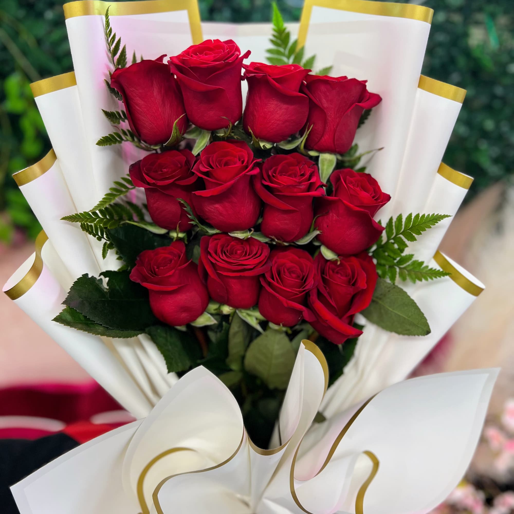 Hand-tied bouquet of red roses wrapped in white paper with gold trim