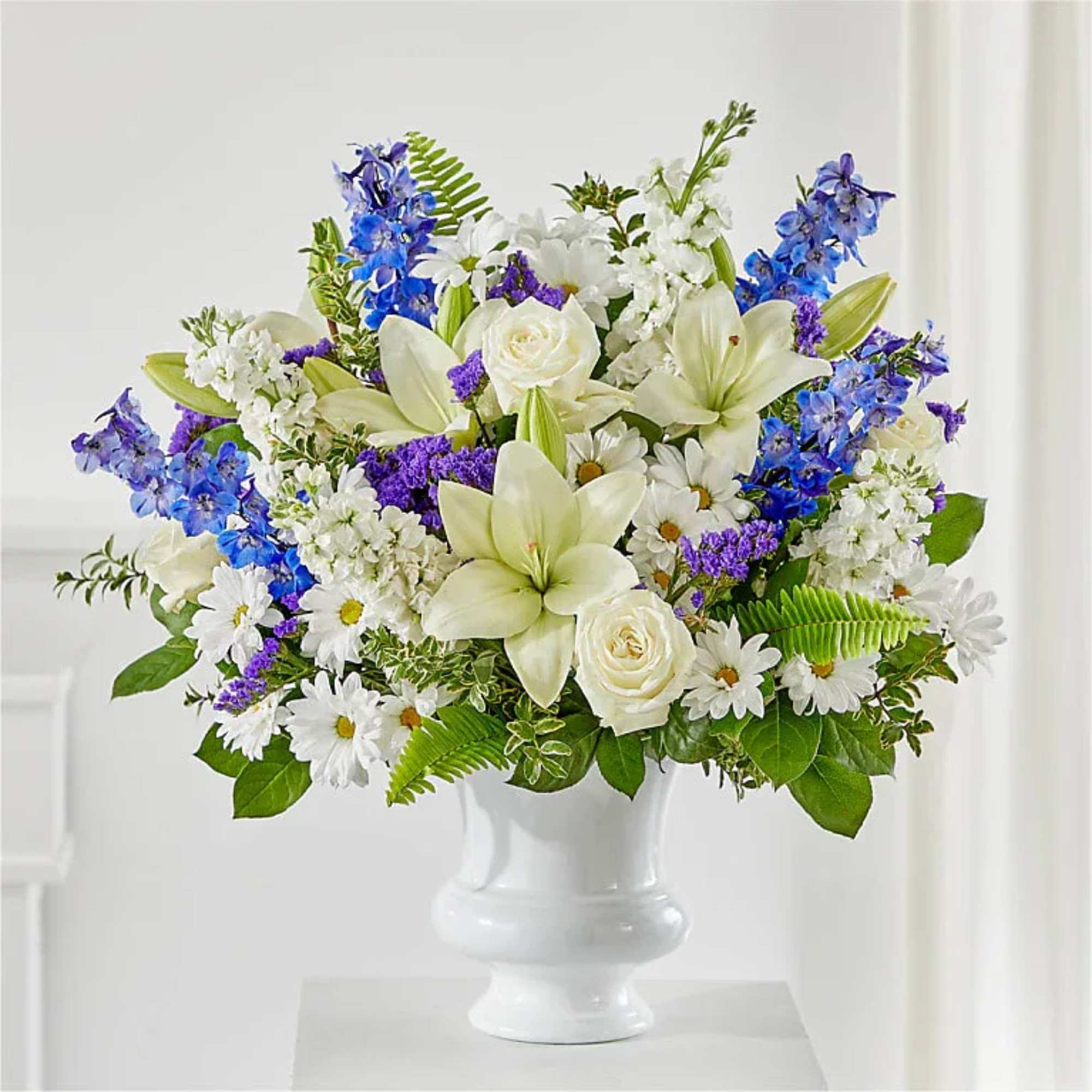 White lilies, roses, daisies, and blue flowers in a white vase