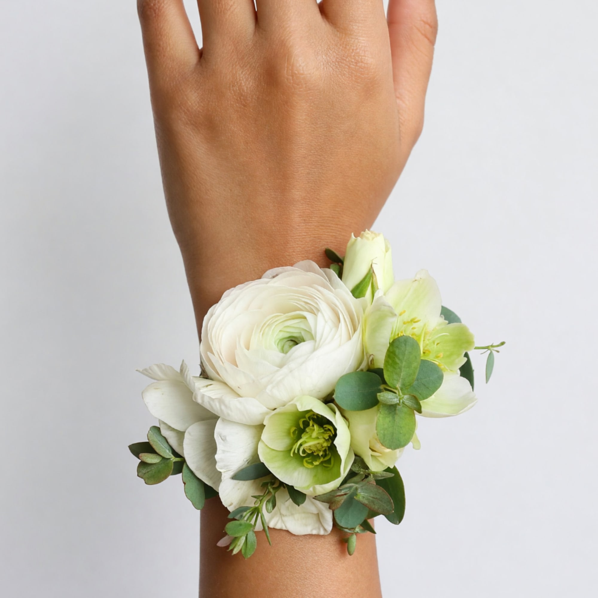 White floral wrist corsage with green accents on a person's wrist