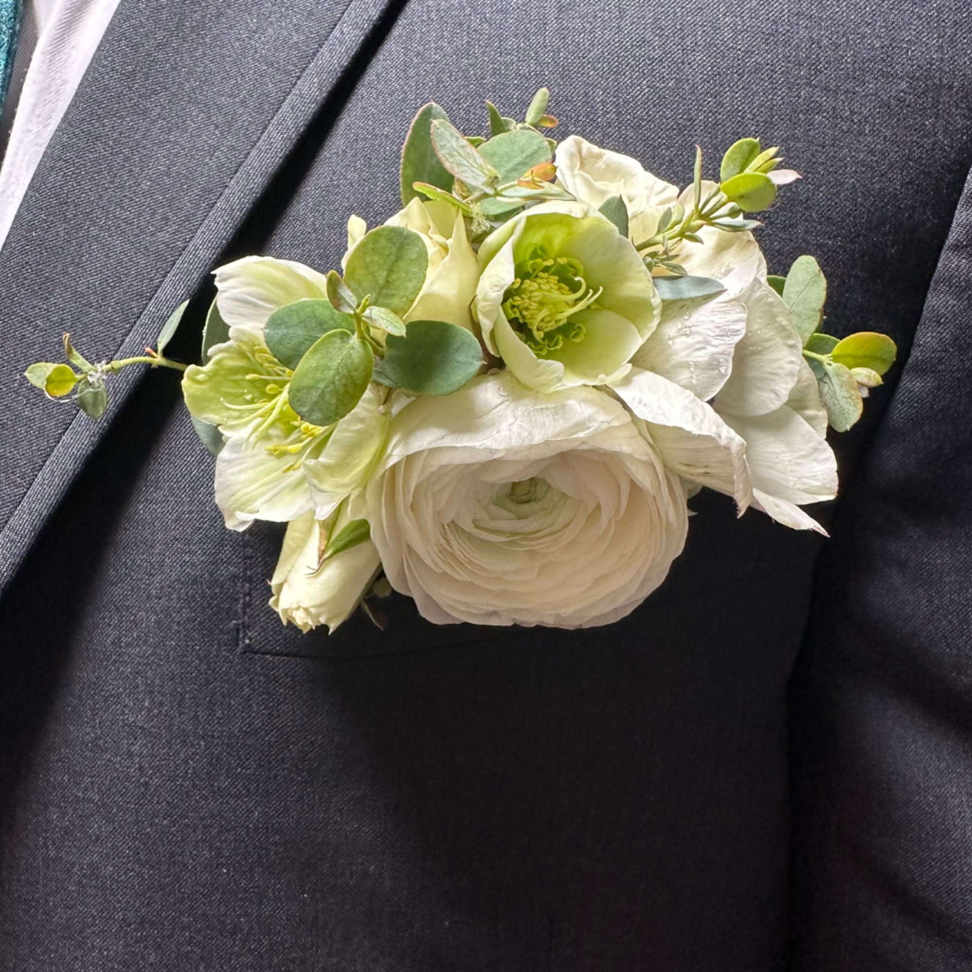 White boutonniere with green flowers and eucalyptus on a dark suit lapel