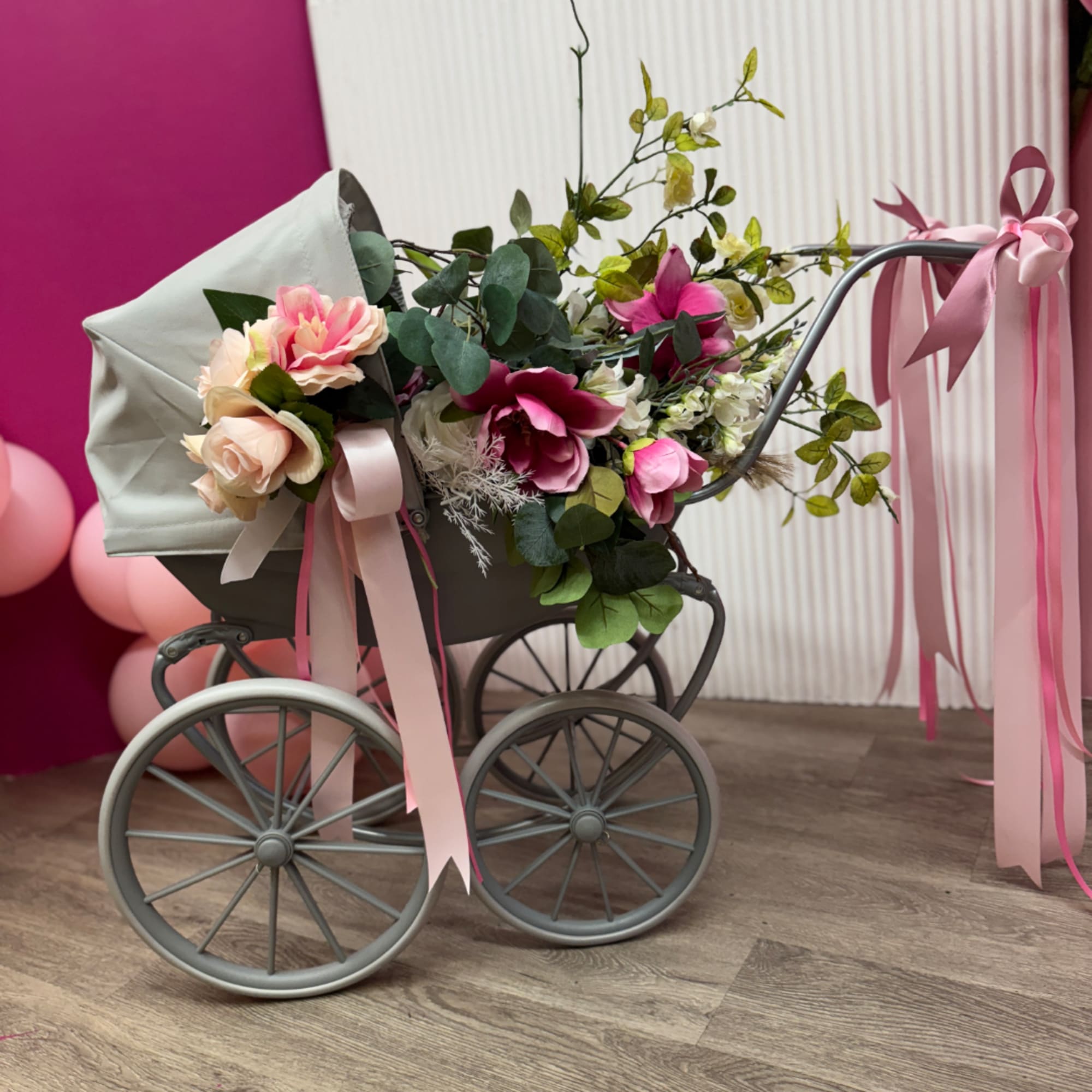 Floral arrangement in a gray baby carriage with pink ribbons