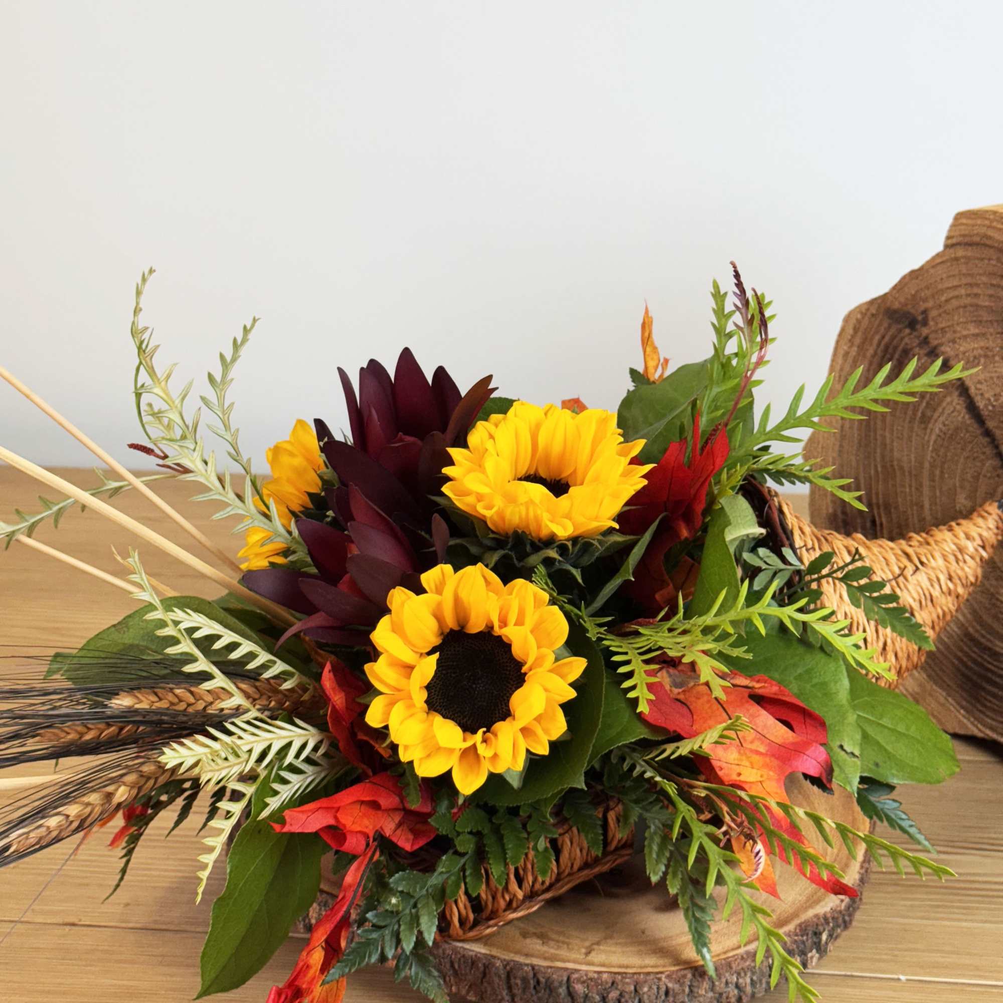 Cornucopia basket with bright yellow sunflowers and burgundy blooms in a fall arrangement.