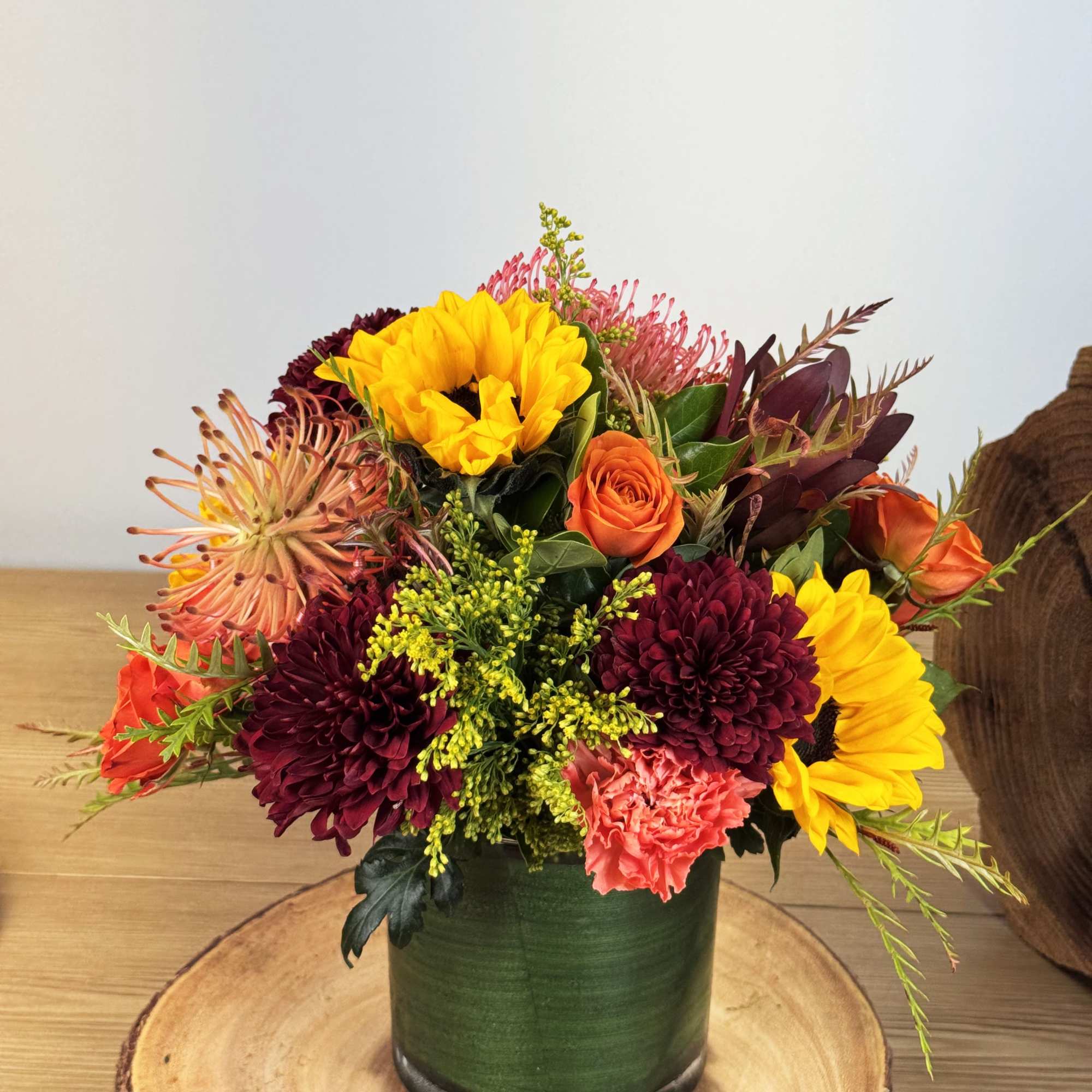 Mixed bouquet in a green vase with sunflowers, roses, and chrysanthemums