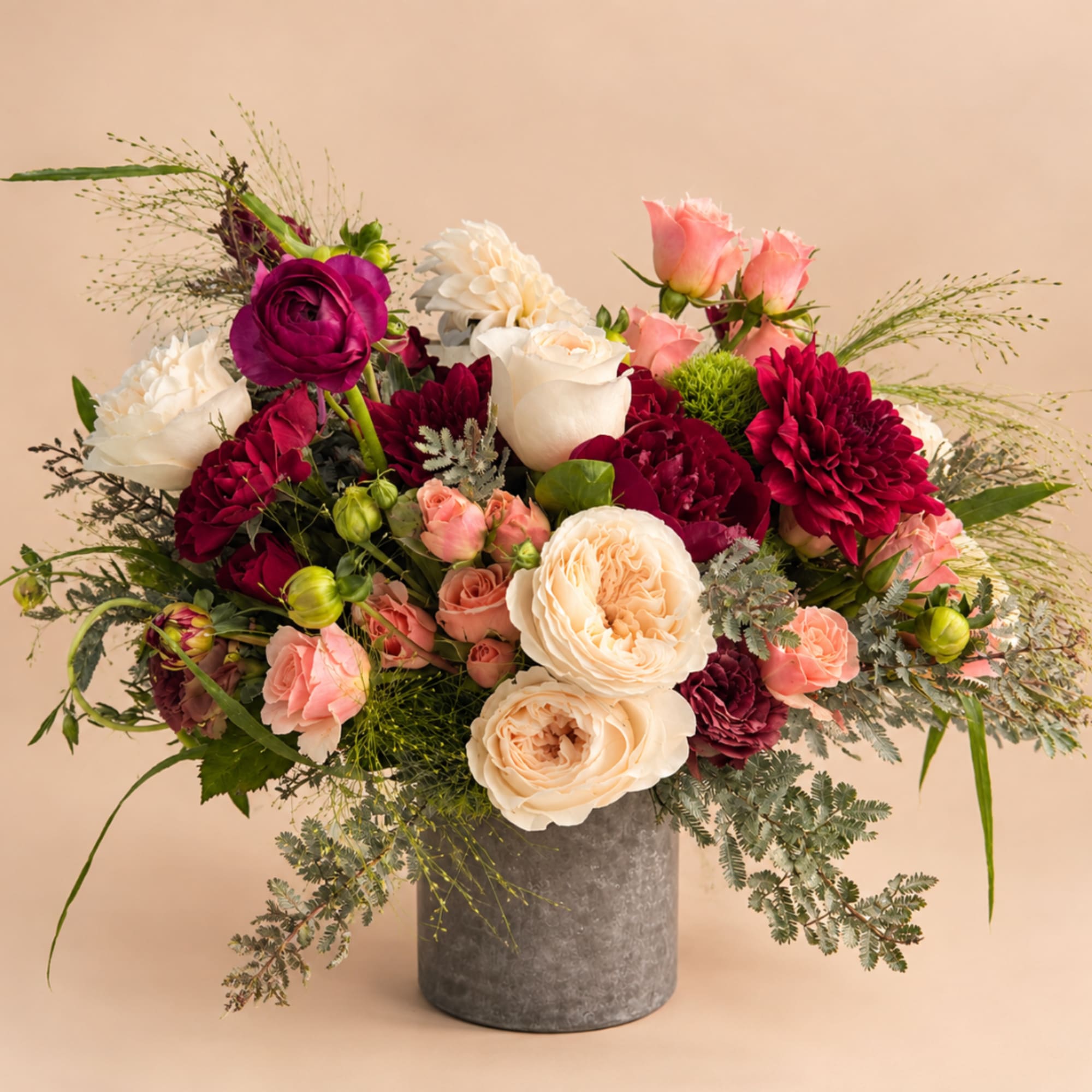 Mixed bouquet of cream, pink, and burgundy flowers in a gray vase