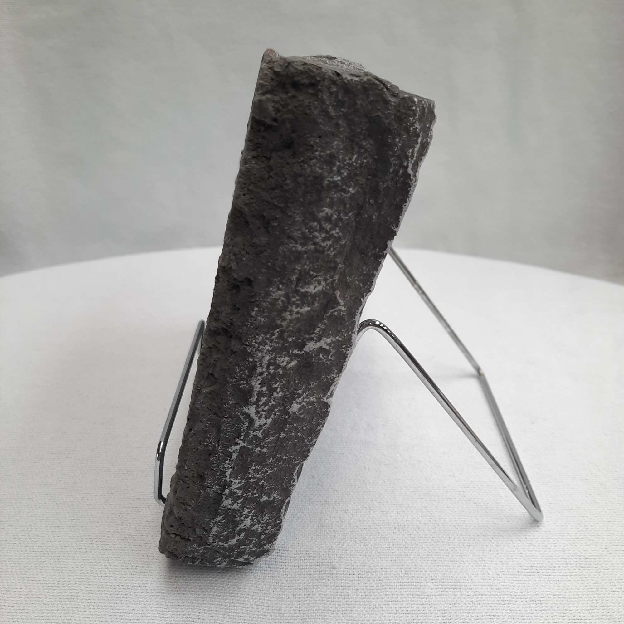 Dark rough stone fragment on a metal display stand