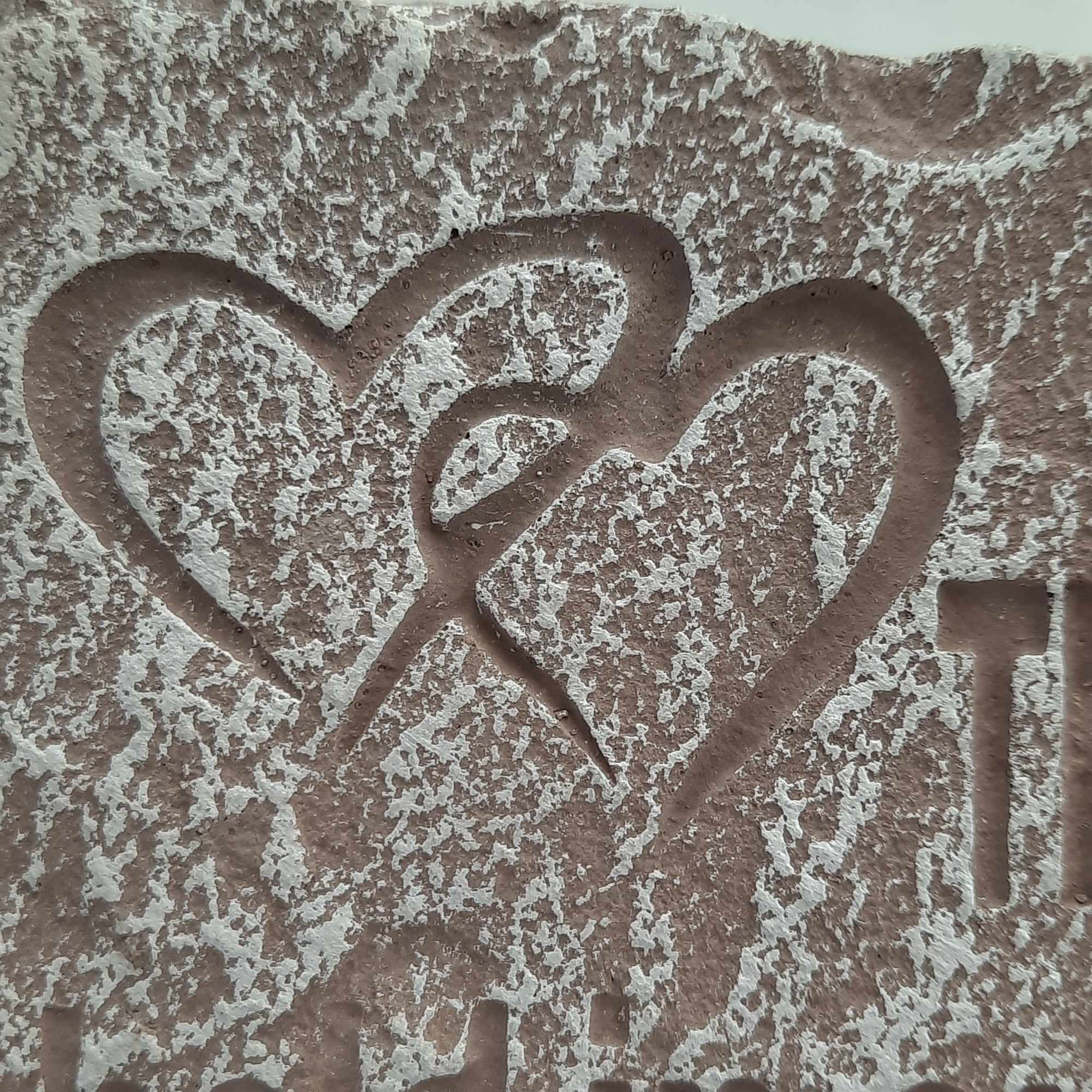 Textured stone surface with carved heart shapes and partial lettering