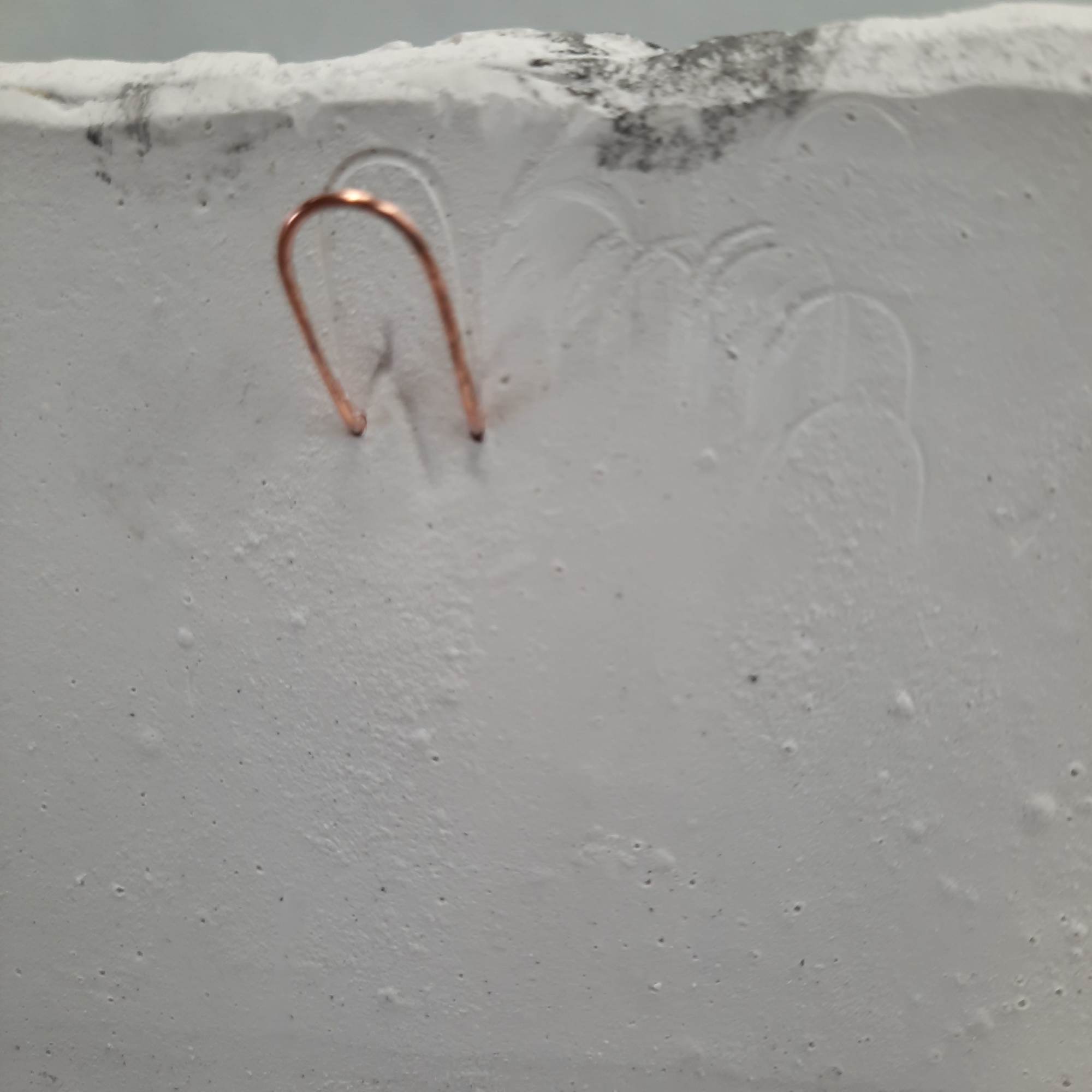 A copper U-shaped hook embedded in a white textured surface