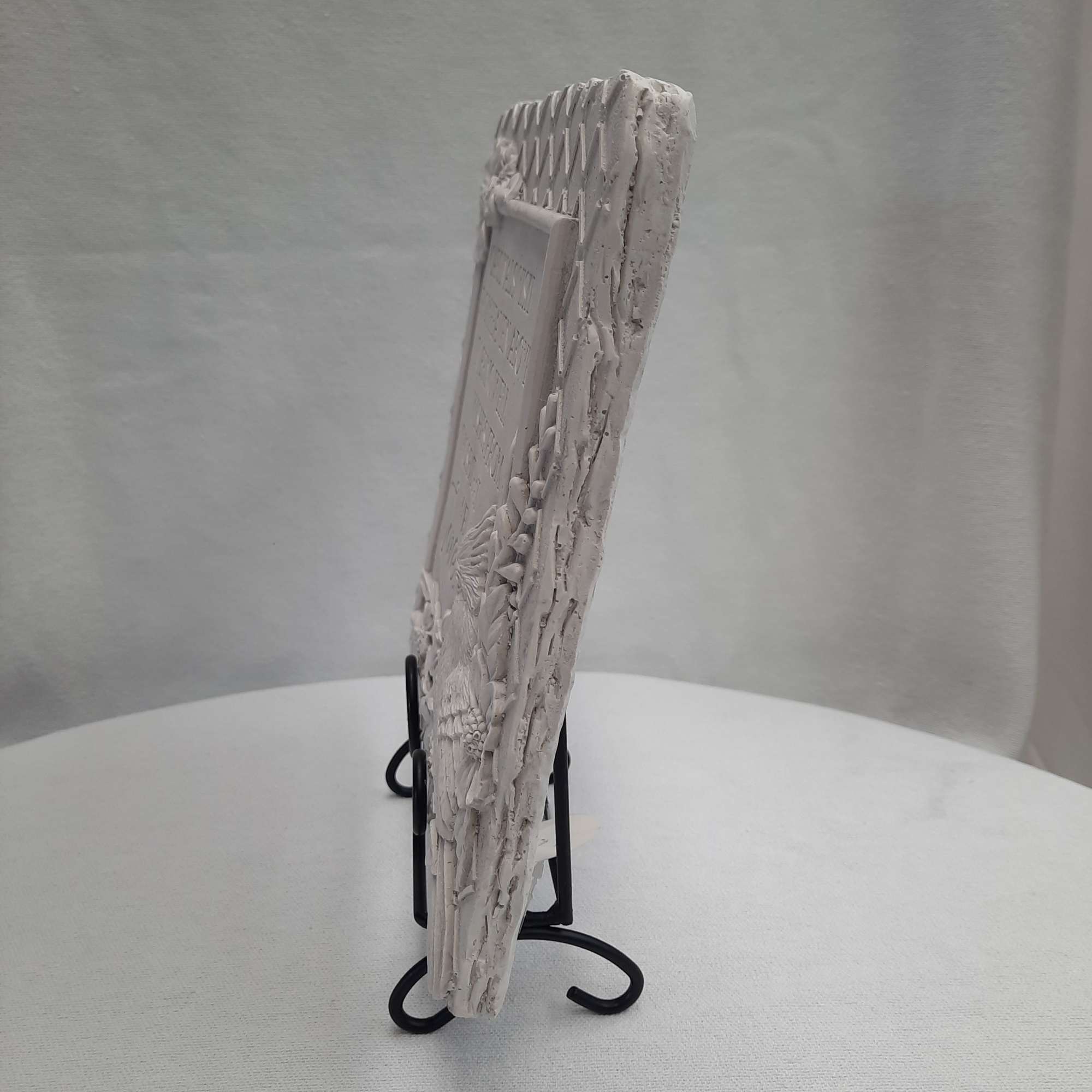 White carved decorative plaque on a black metal stand