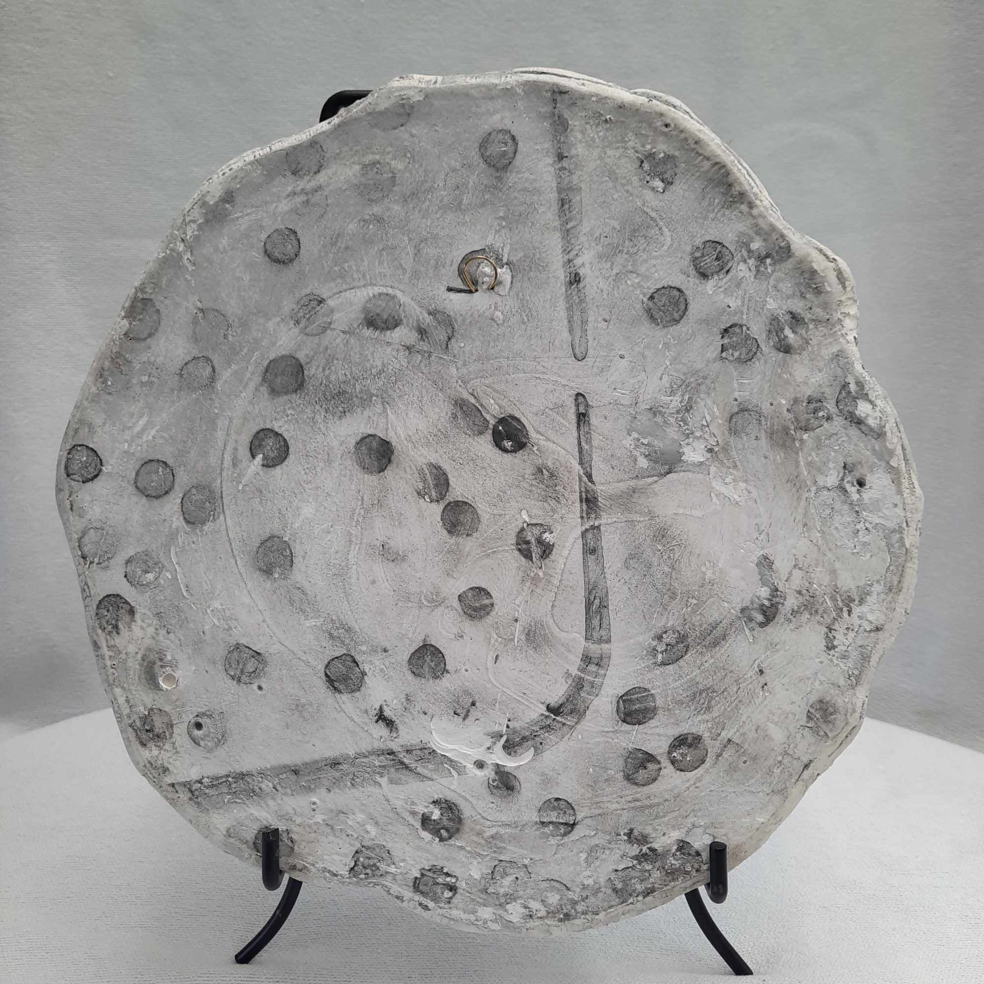 Round gray decorative wall plaque with raised dot texture on a stand