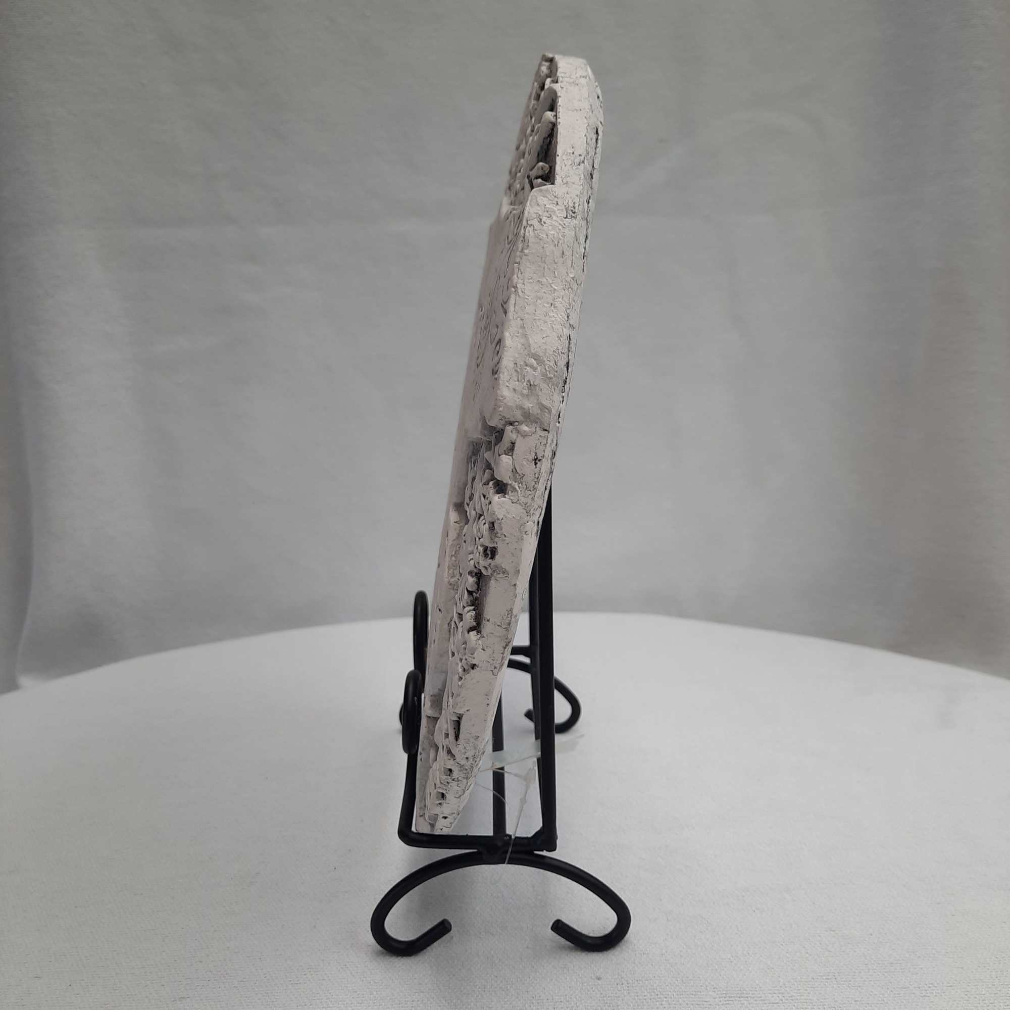 White textured decorative plaque on a black metal stand