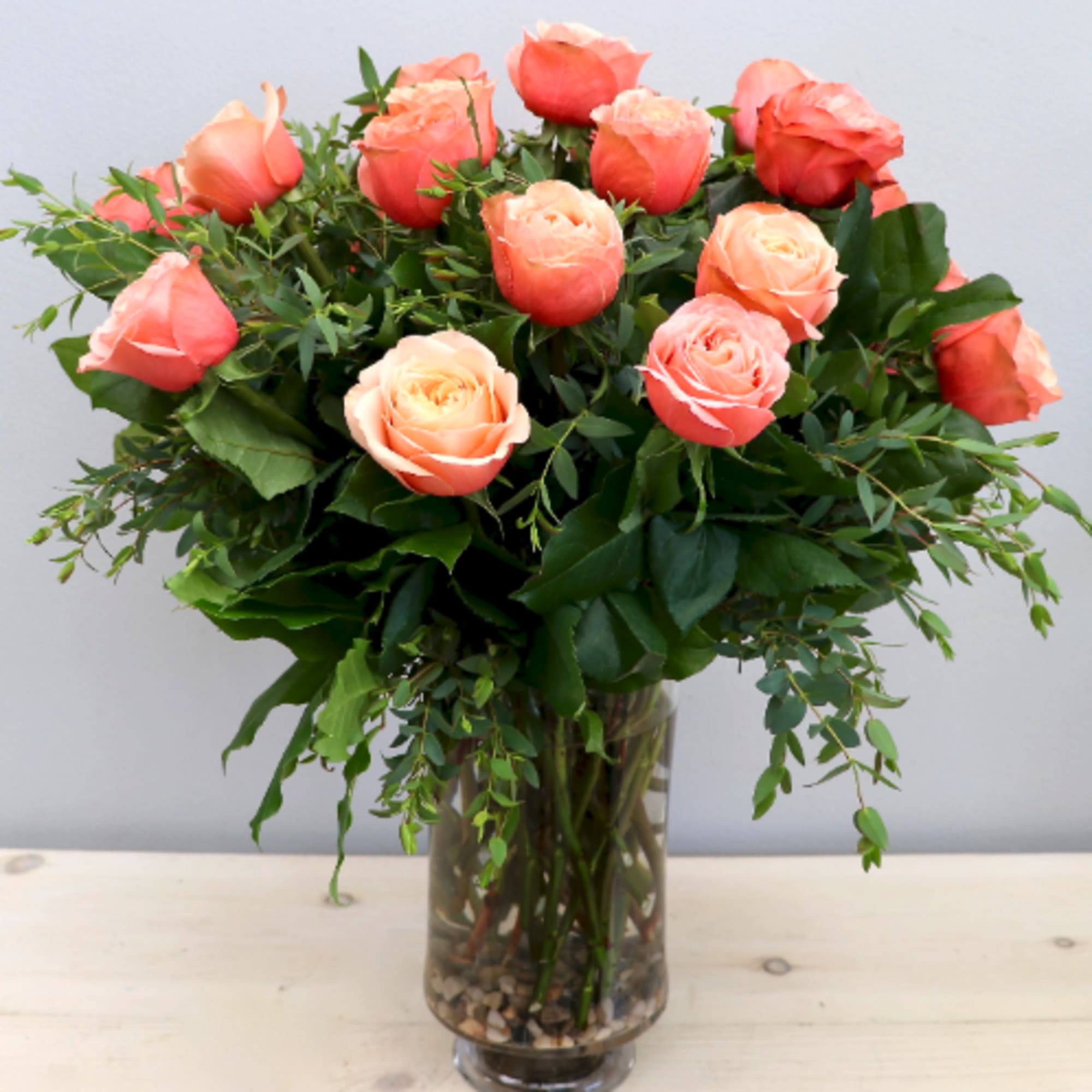 Peach and coral roses arranged in a clear glass vase filled with stones