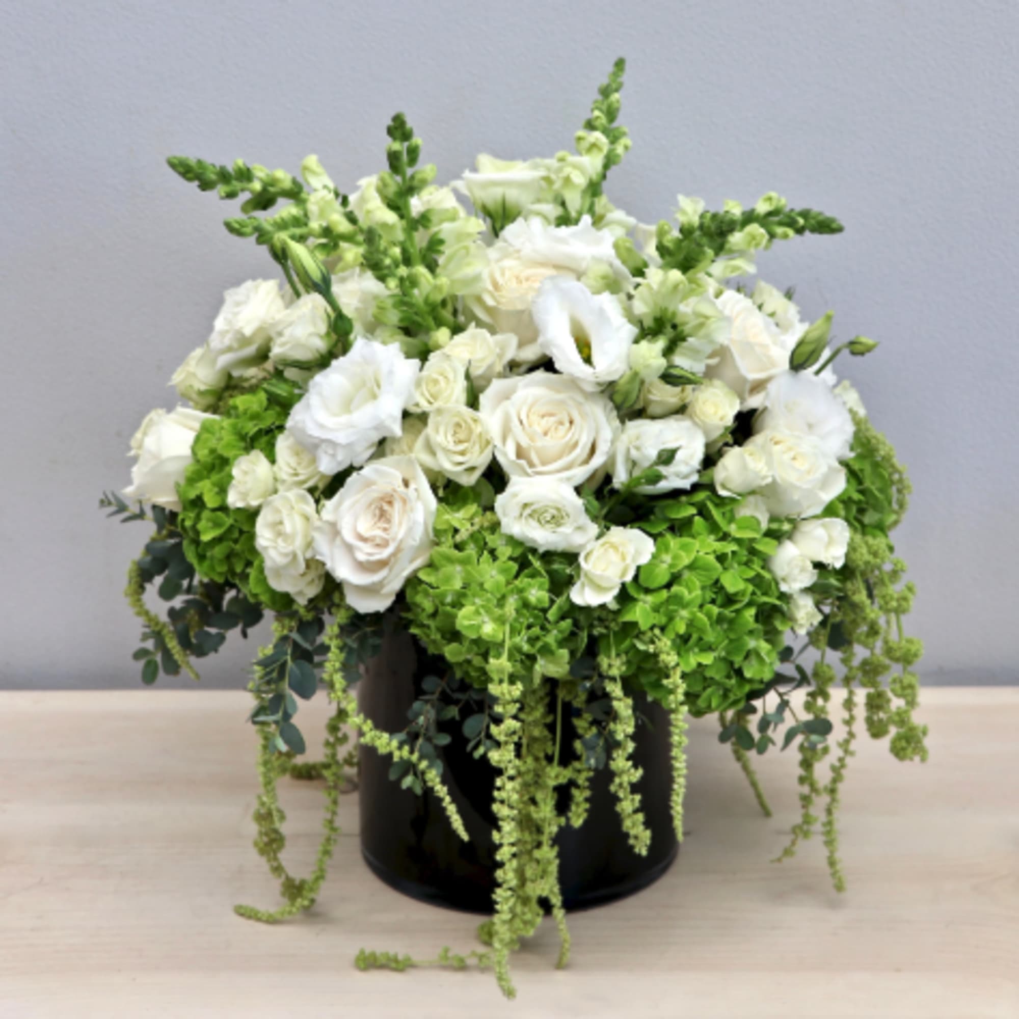 Round arrangement of white roses and lisianthus with green hydrangeas in a black cylinder vase