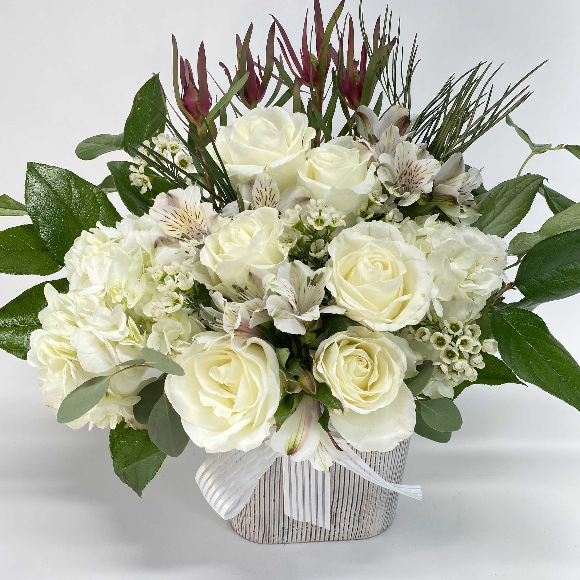 White roses and hydrangeas in a striped vase with a ribbon