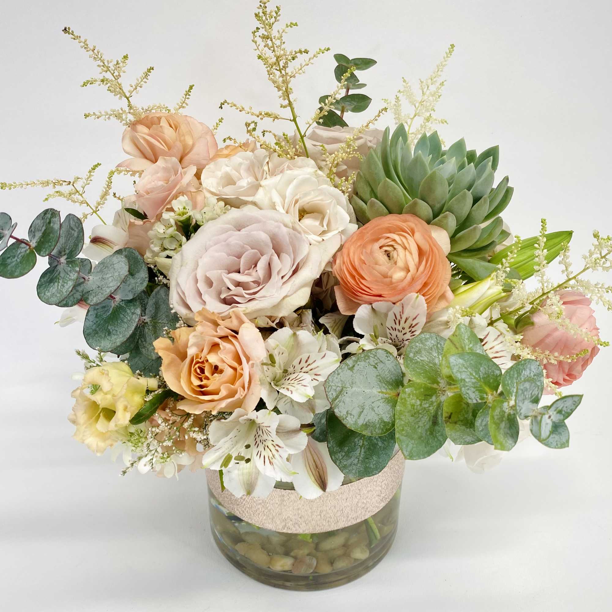Mixed pastel bouquet in a glass vase with eucalyptus and succulents