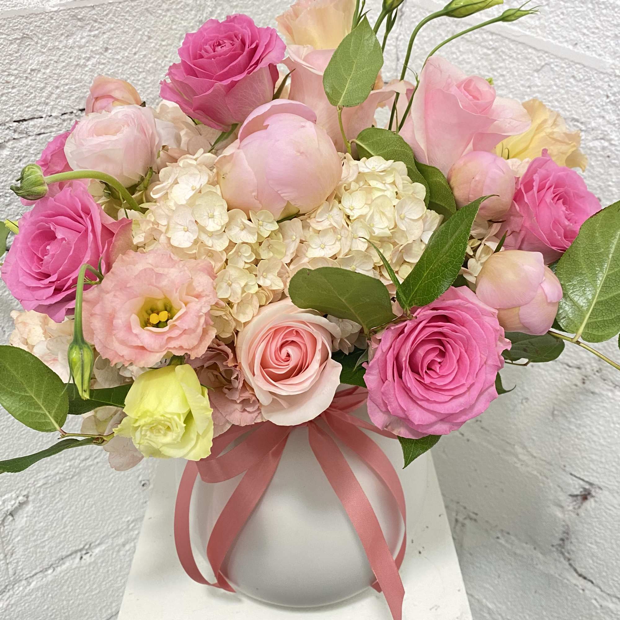 Pink and cream roses with hydrangea in a white vase tied with ribbon