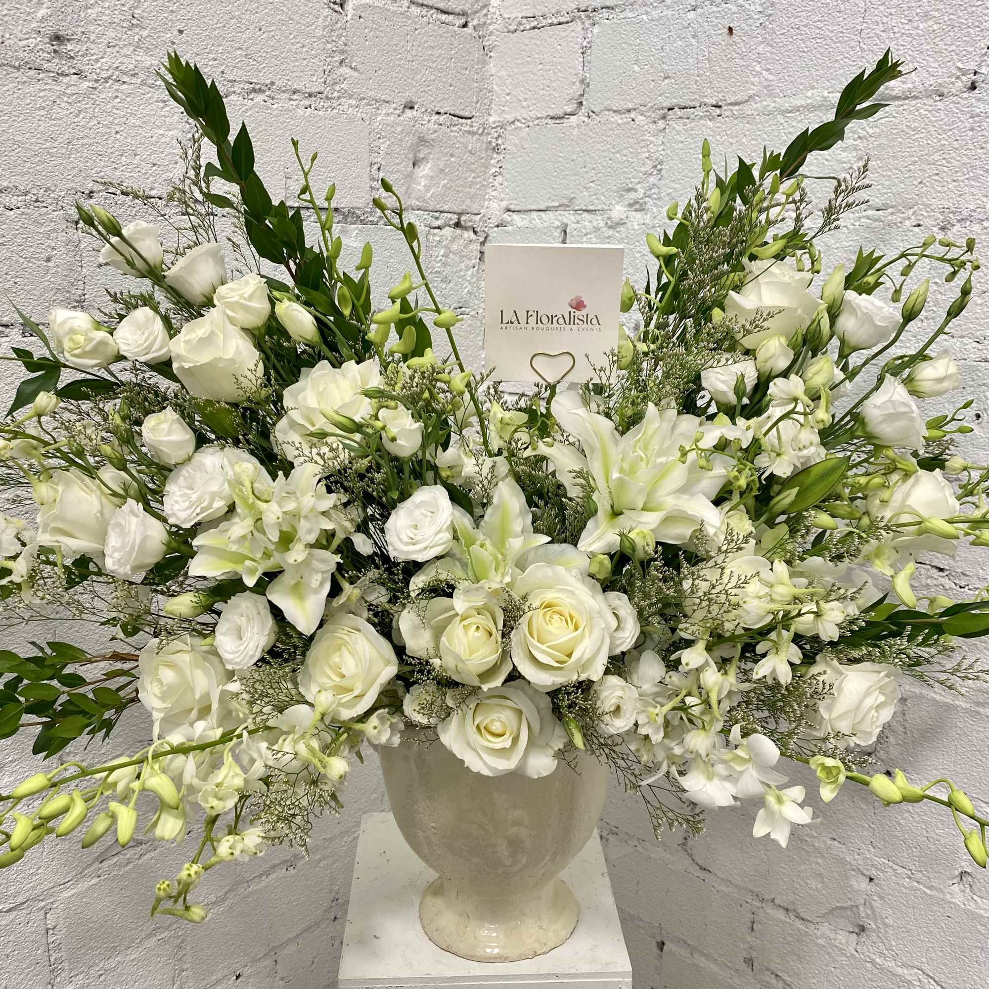 White floral arrangement in a cream urn vase with roses and lilies
