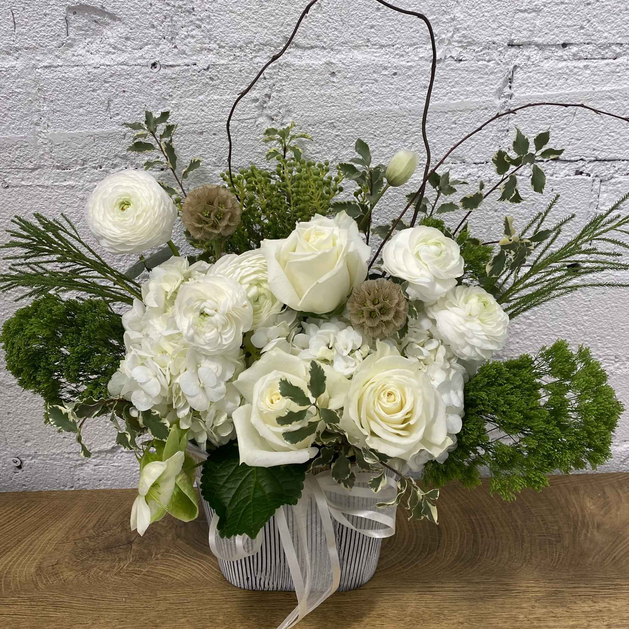 White roses and ranunculus arranged in a striped basket with ribbon