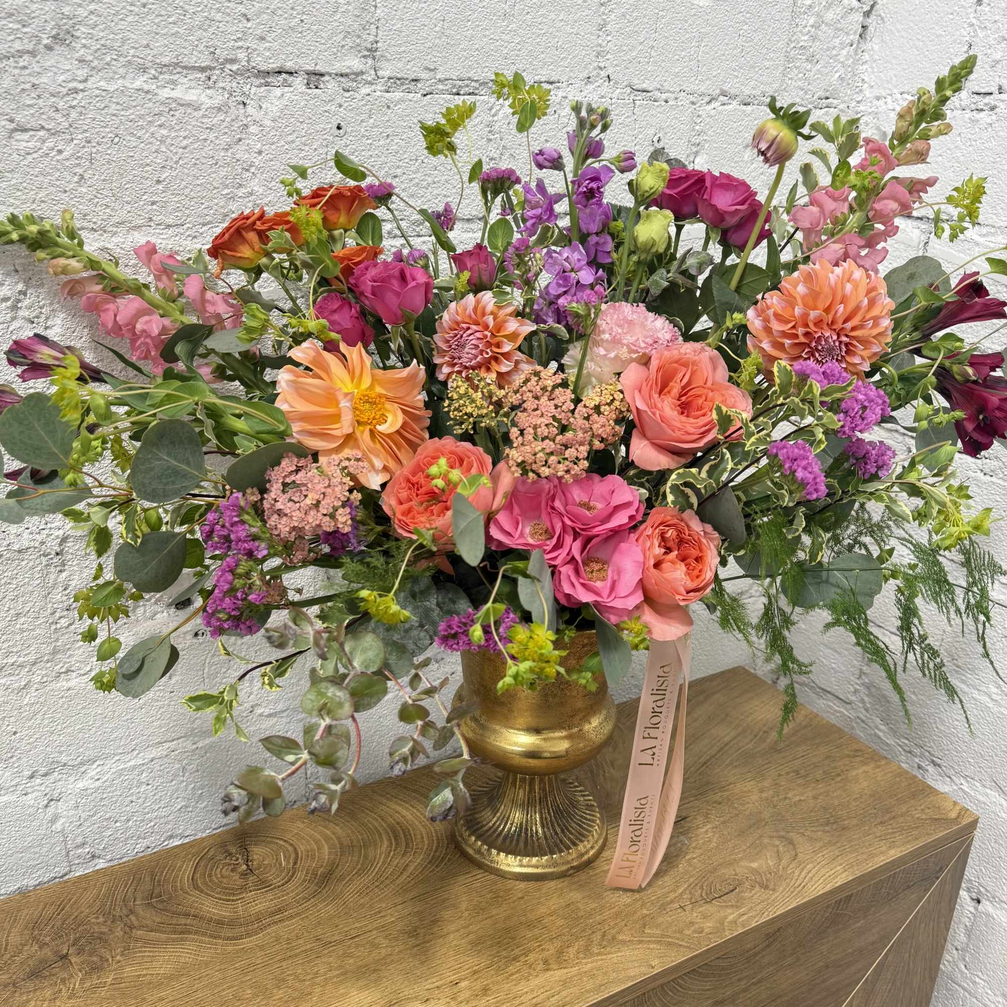 Large mixed bouquet in a gold vase with pink, orange, and purple flowers