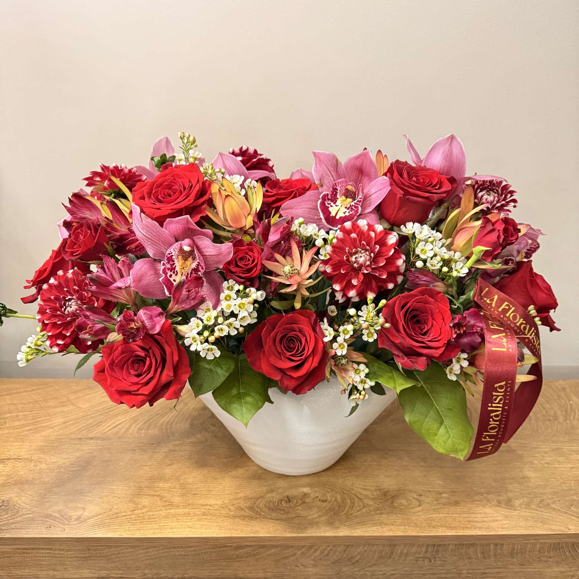 Red roses and pink orchids arranged in a white bowl vase, photo 2 of 2
