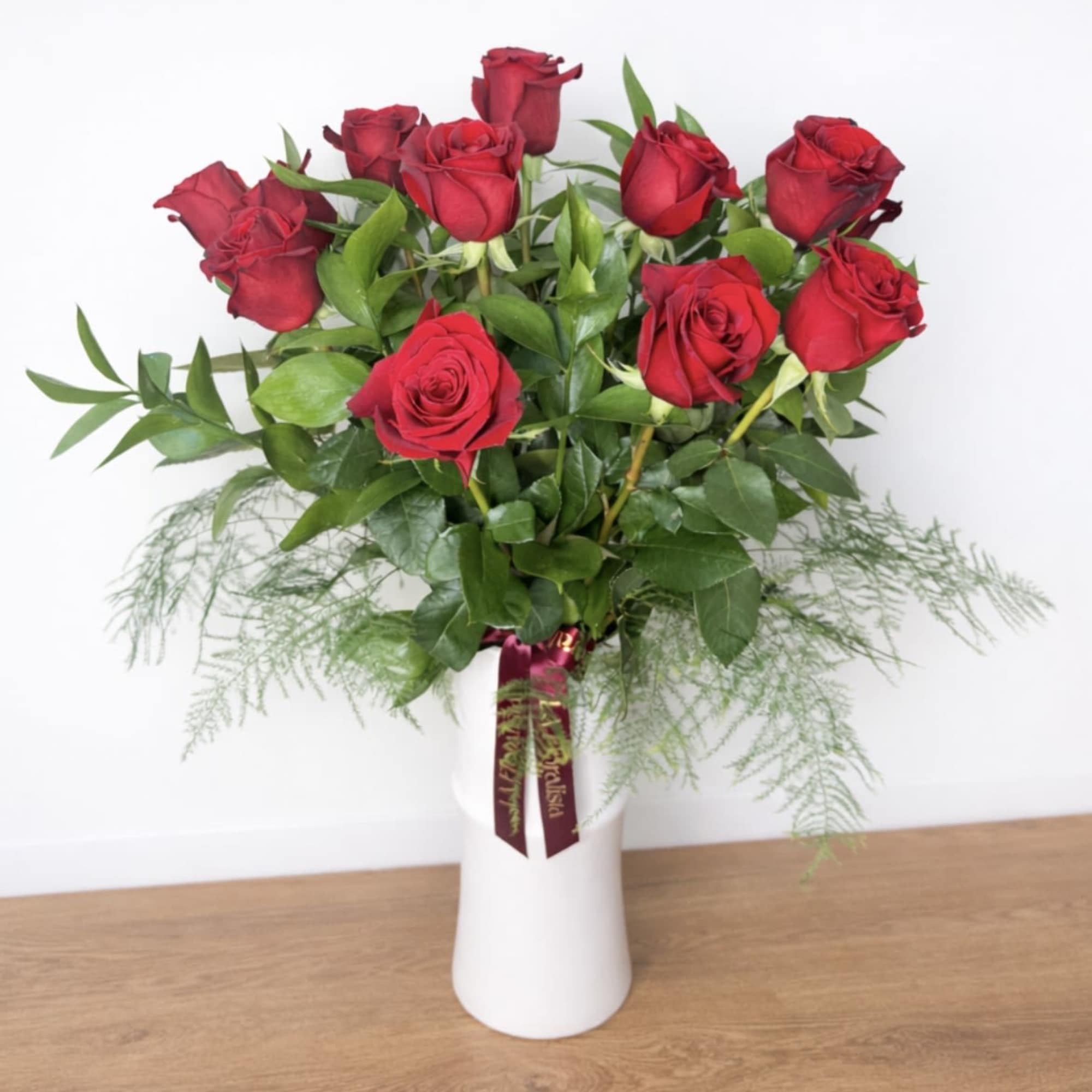 Red roses arranged in a white vase with greenery
