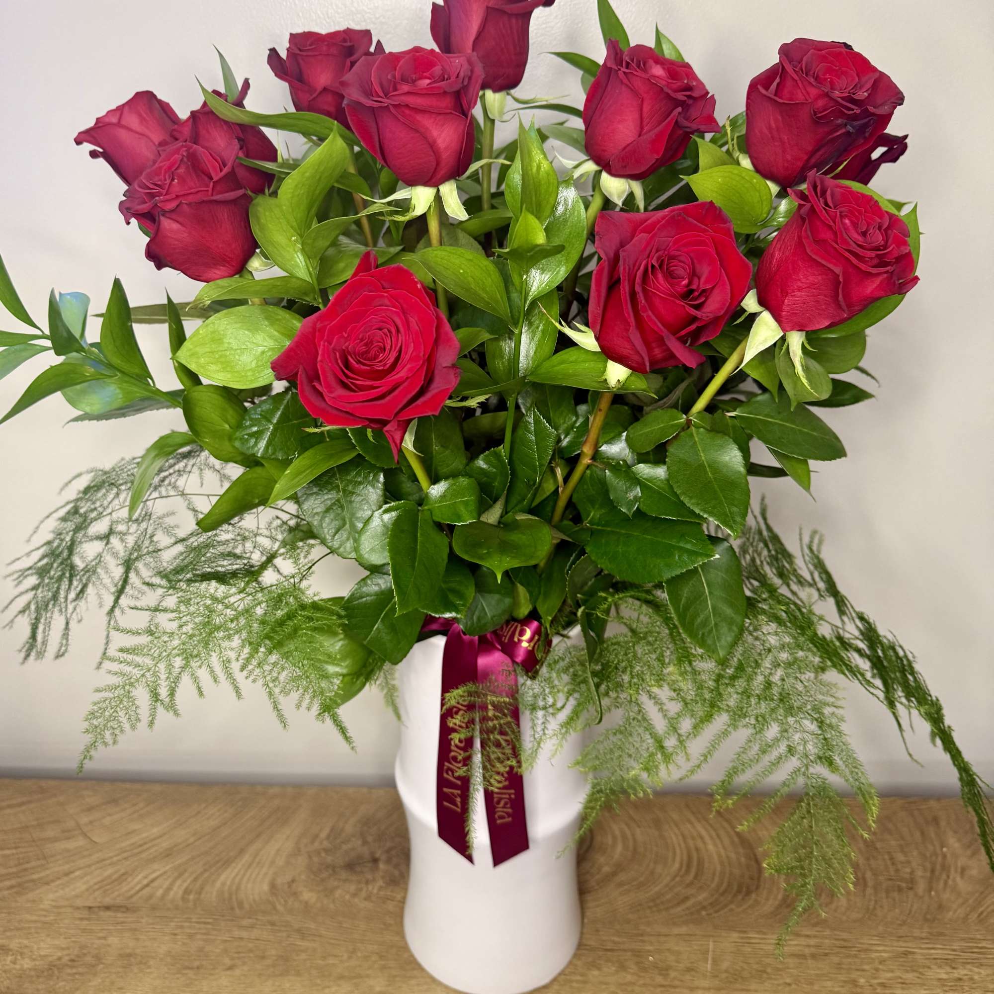 Red roses arranged in a white vase with trailing greenery.