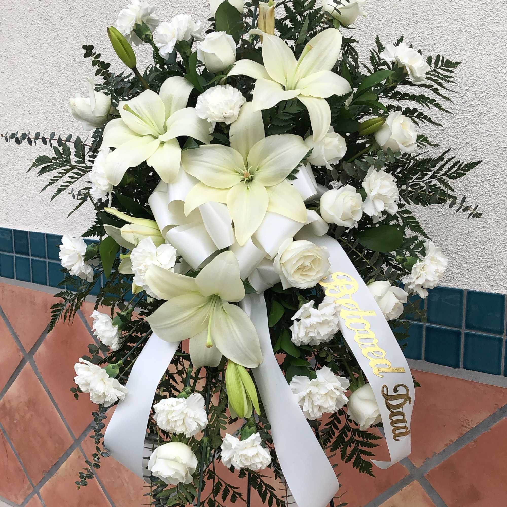 White funeral spray with lilies, roses, carnations, and ribbon on an easel