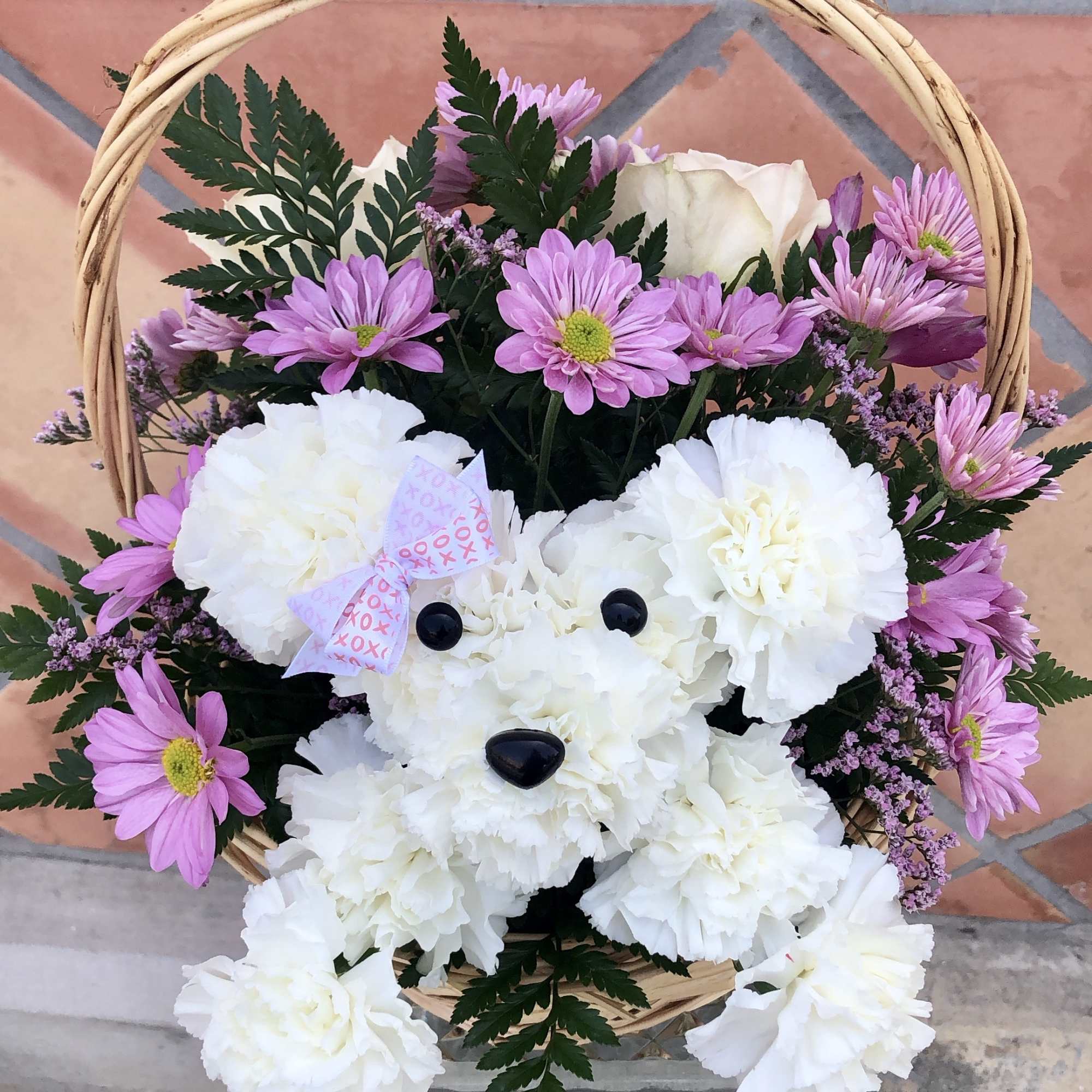 White carnation teddy bear arrangement in a wicker basket with pink daisies