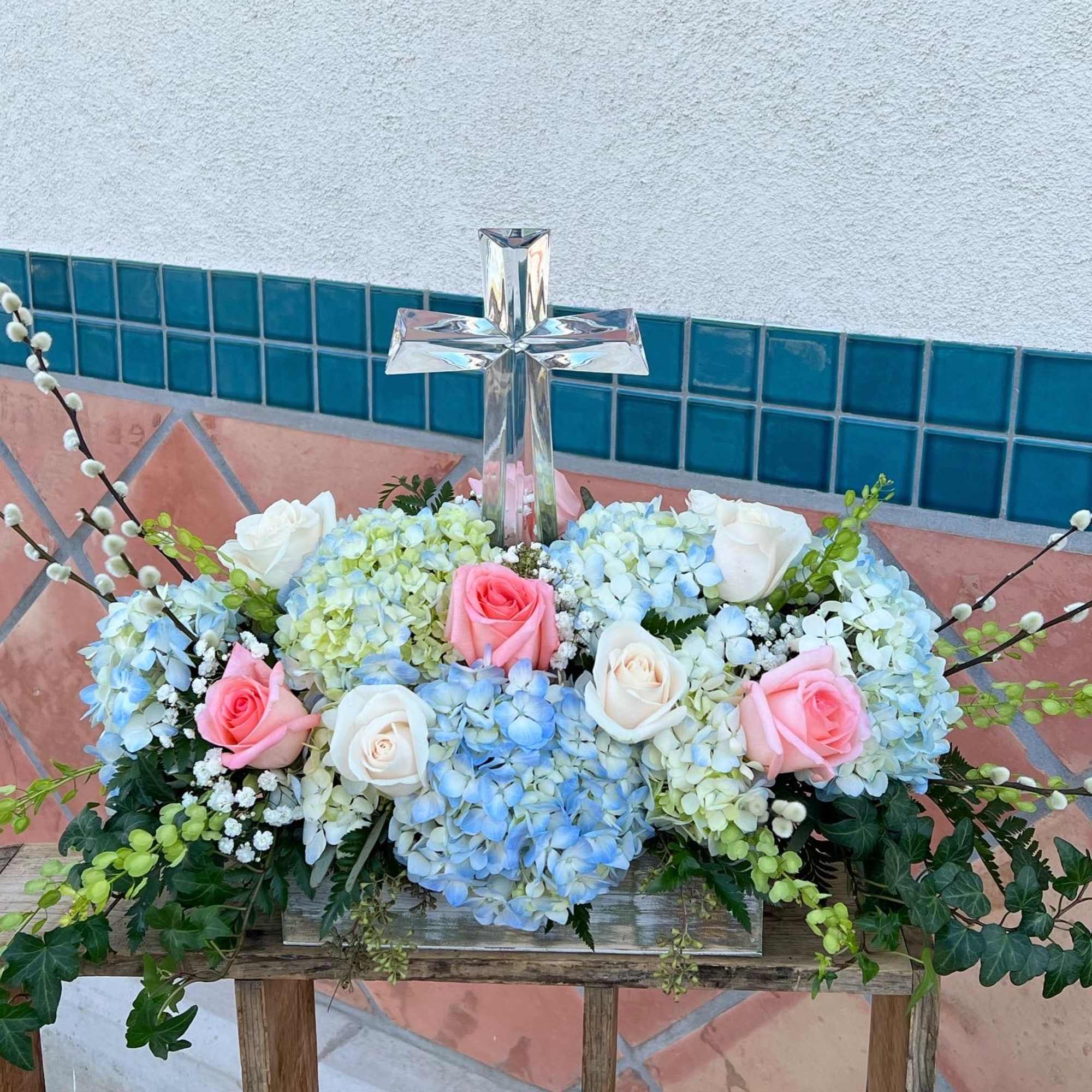 Floral arrangement with roses and hydrangeas around a clear glass cross