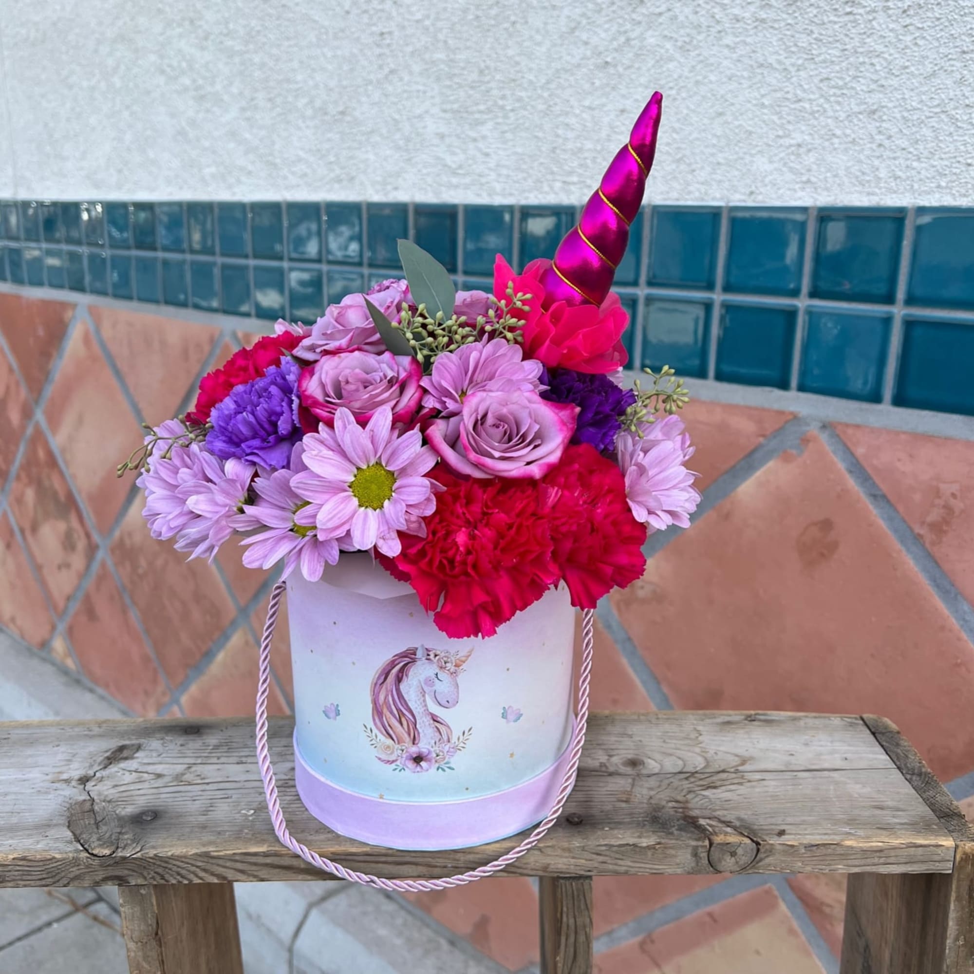 Pink and purple flower arrangement in a unicorn bucket with a horn topper