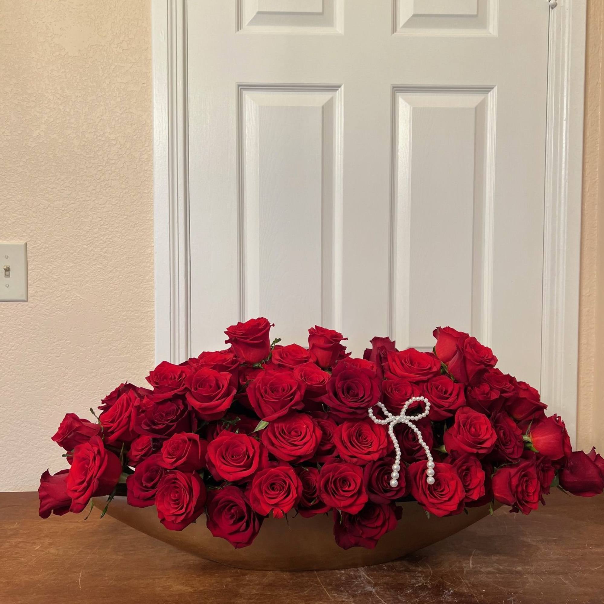 Large arrangement of red roses in a low gold container with a pearl bow