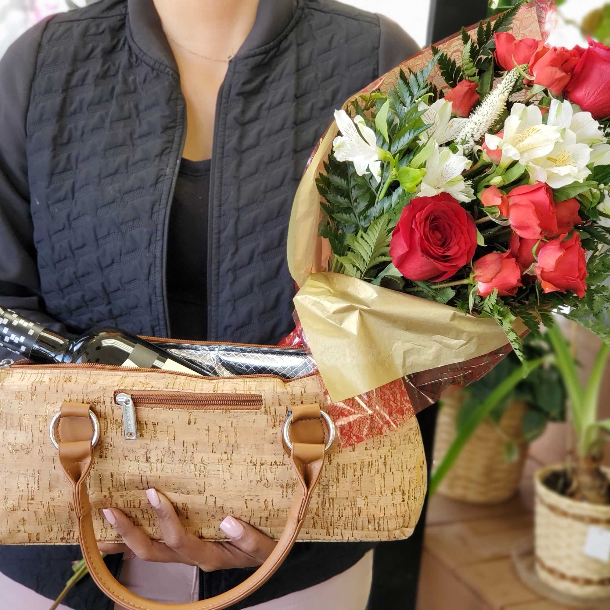 Bouquet of red and white flowers wrapped in gold paper beside a wine bottle in a cork tote.