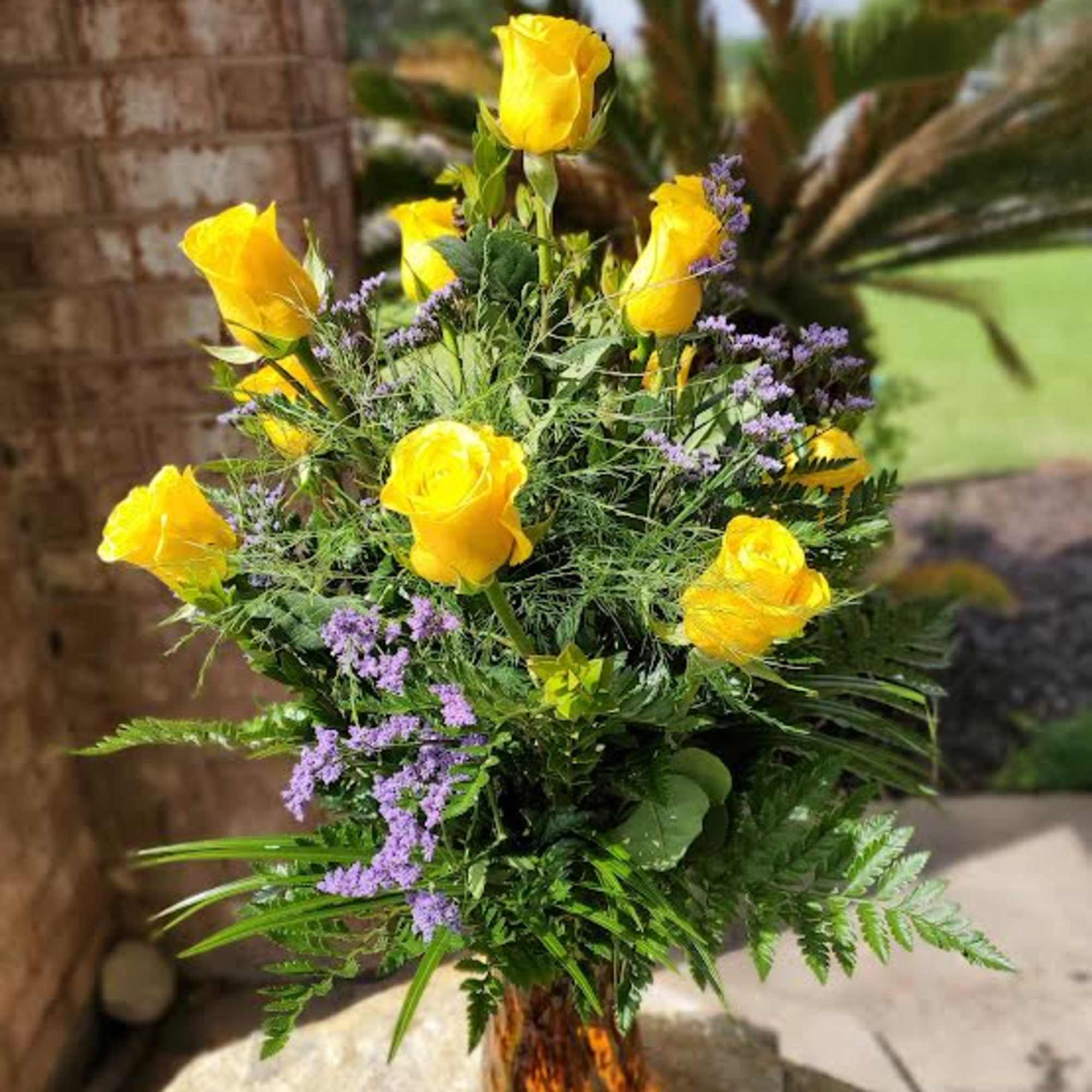 Yellow roses with purple filler in a glass vase