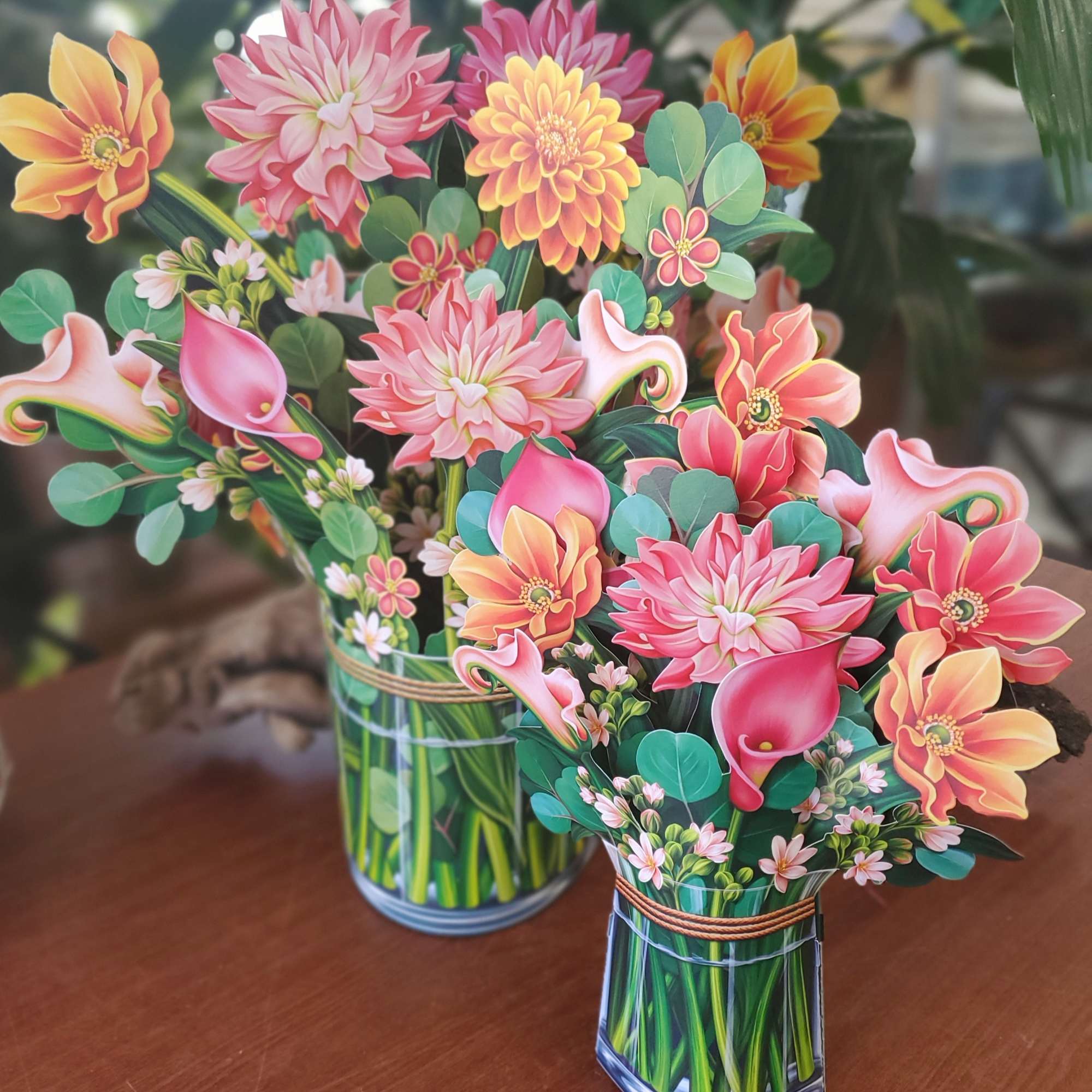 Two colorful paper flower bouquets in glass vases on a table