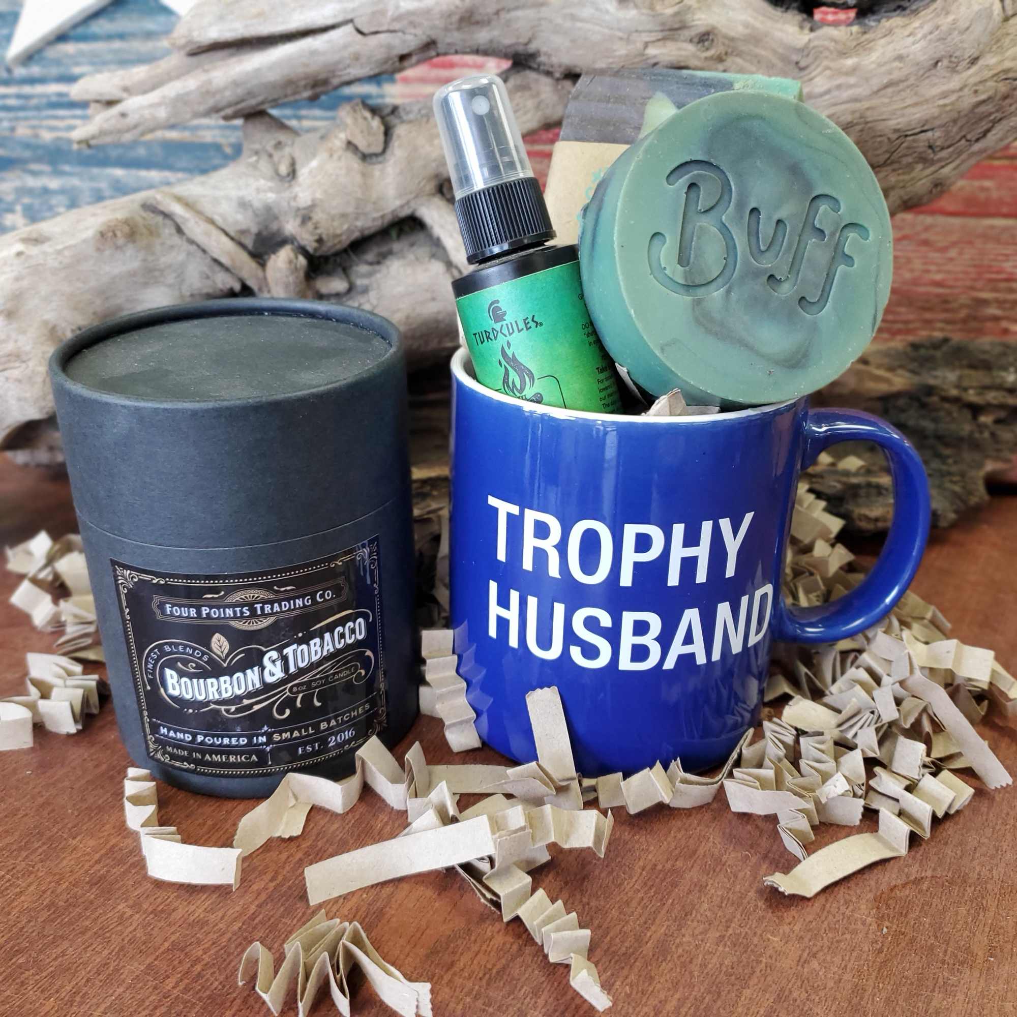 Blue mug with "Trophy Husband" text, candle tin, and soap items in gift packaging