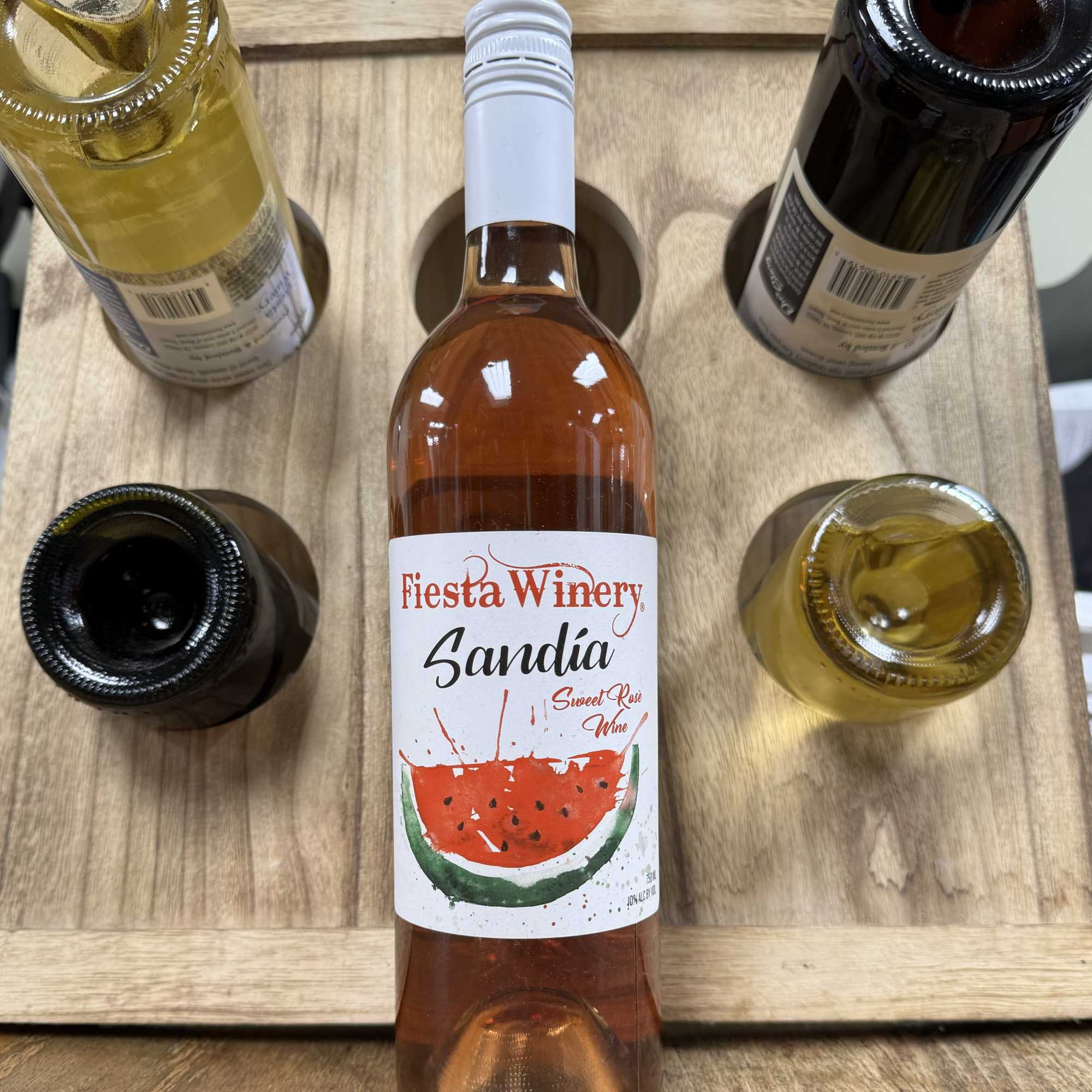 Five wine bottles arranged in a wooden carrier, with a rosé bottle centered