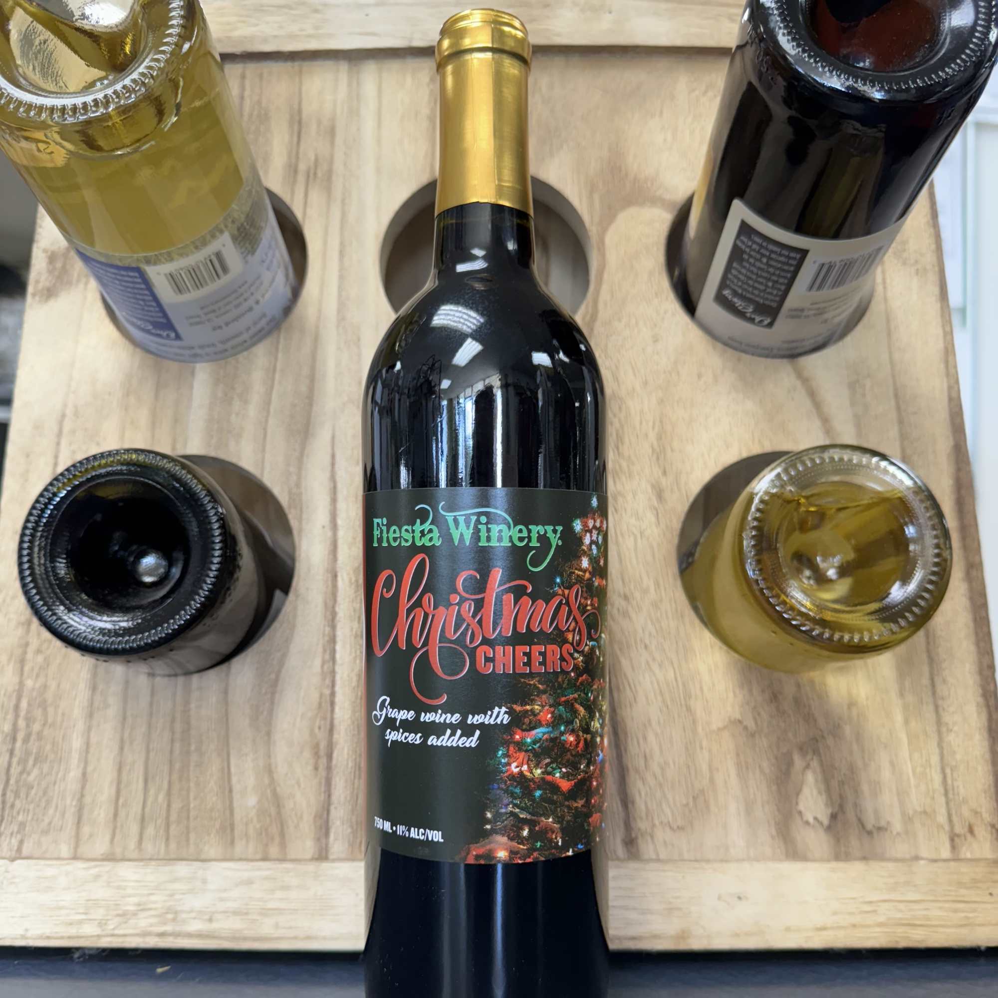 Five wine bottles arranged in a wooden carrier, one labeled Christmas Cheers.