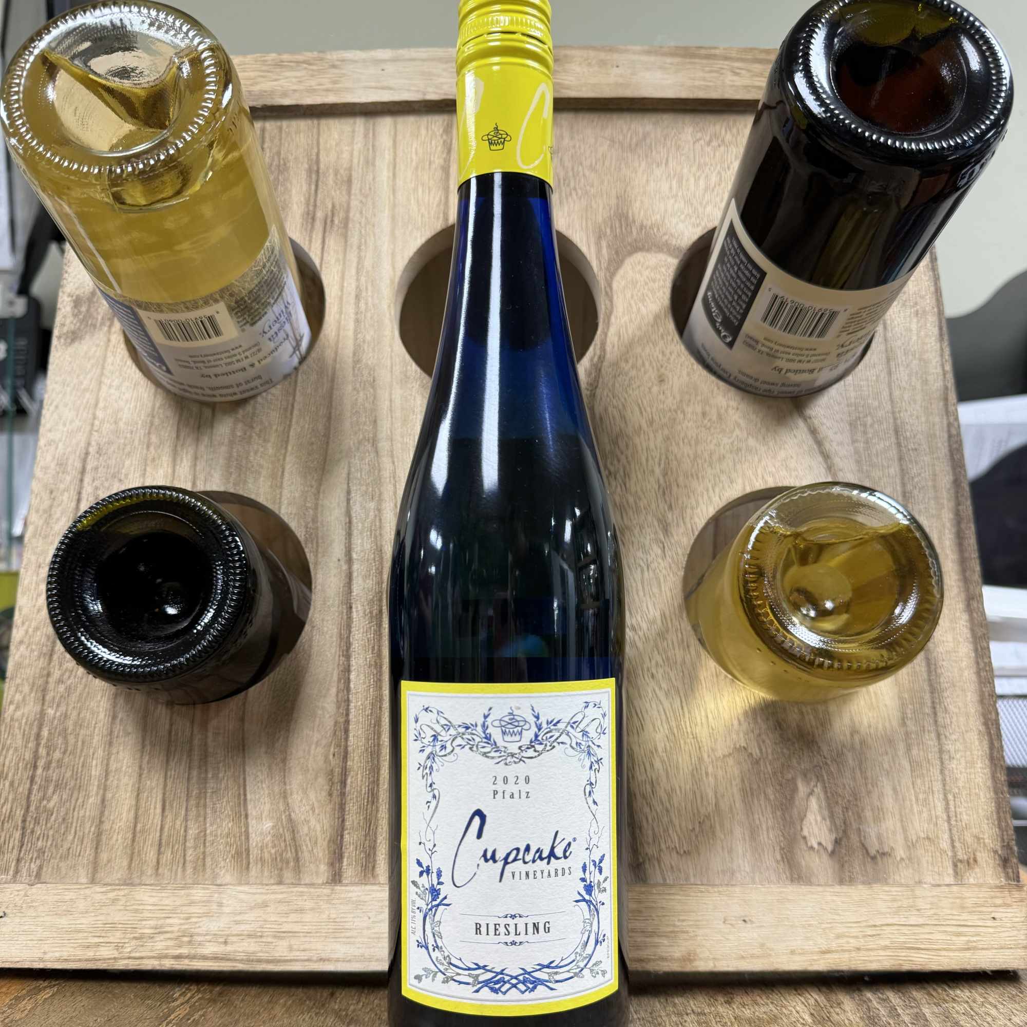 Five wine bottles arranged in a wooden carrier, one upright in the center