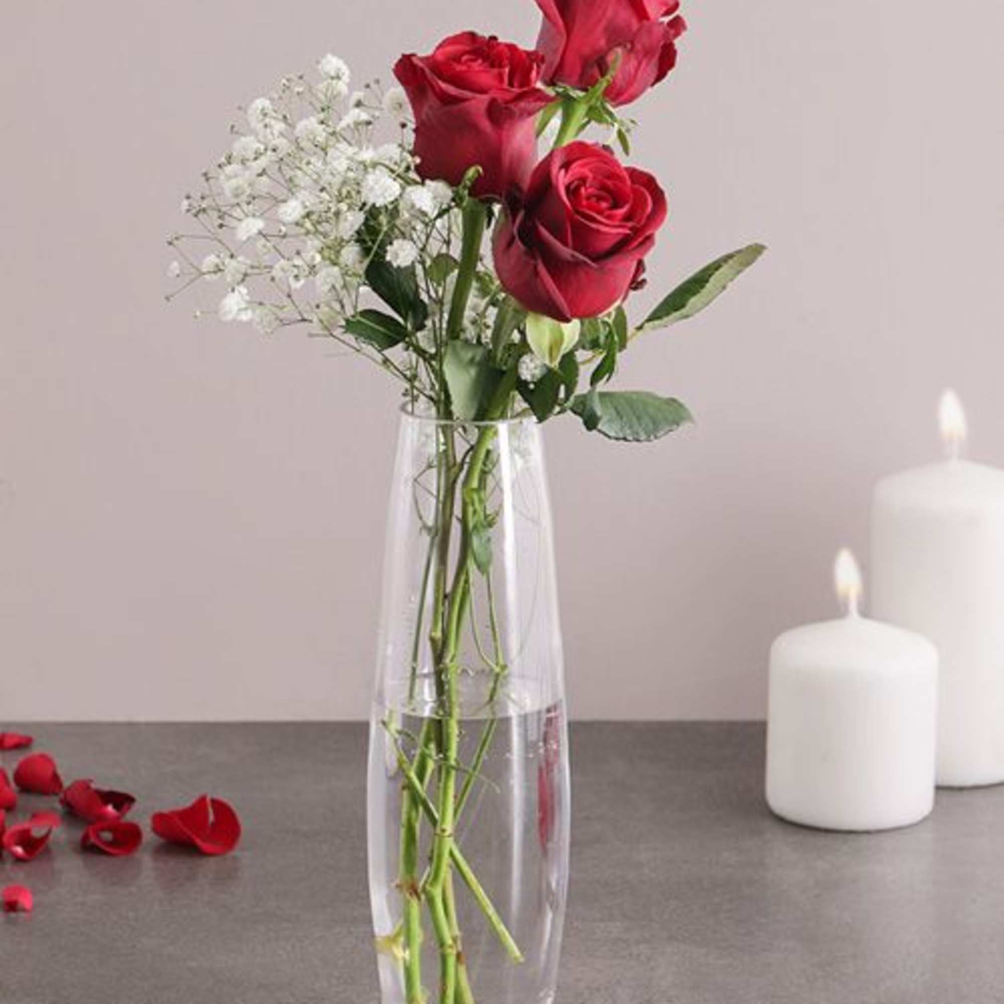 Three red roses in a clear glass vase with white baby's breath