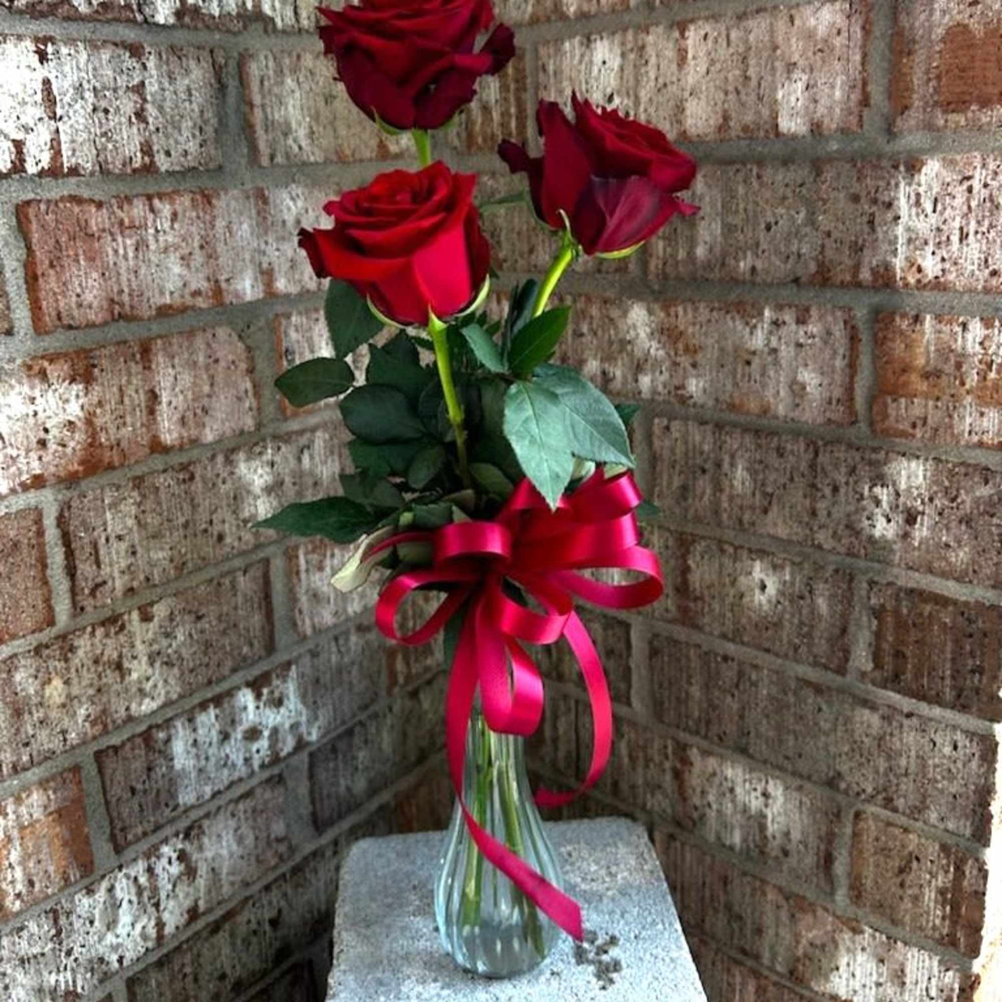Three red roses in a clear glass vase with a pink ribbon