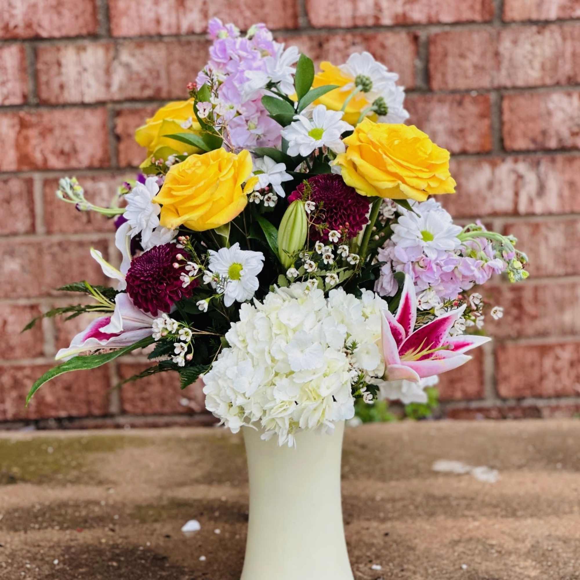 Mixed bouquet of yellow roses, white daisies, and pink lilies in a white vase