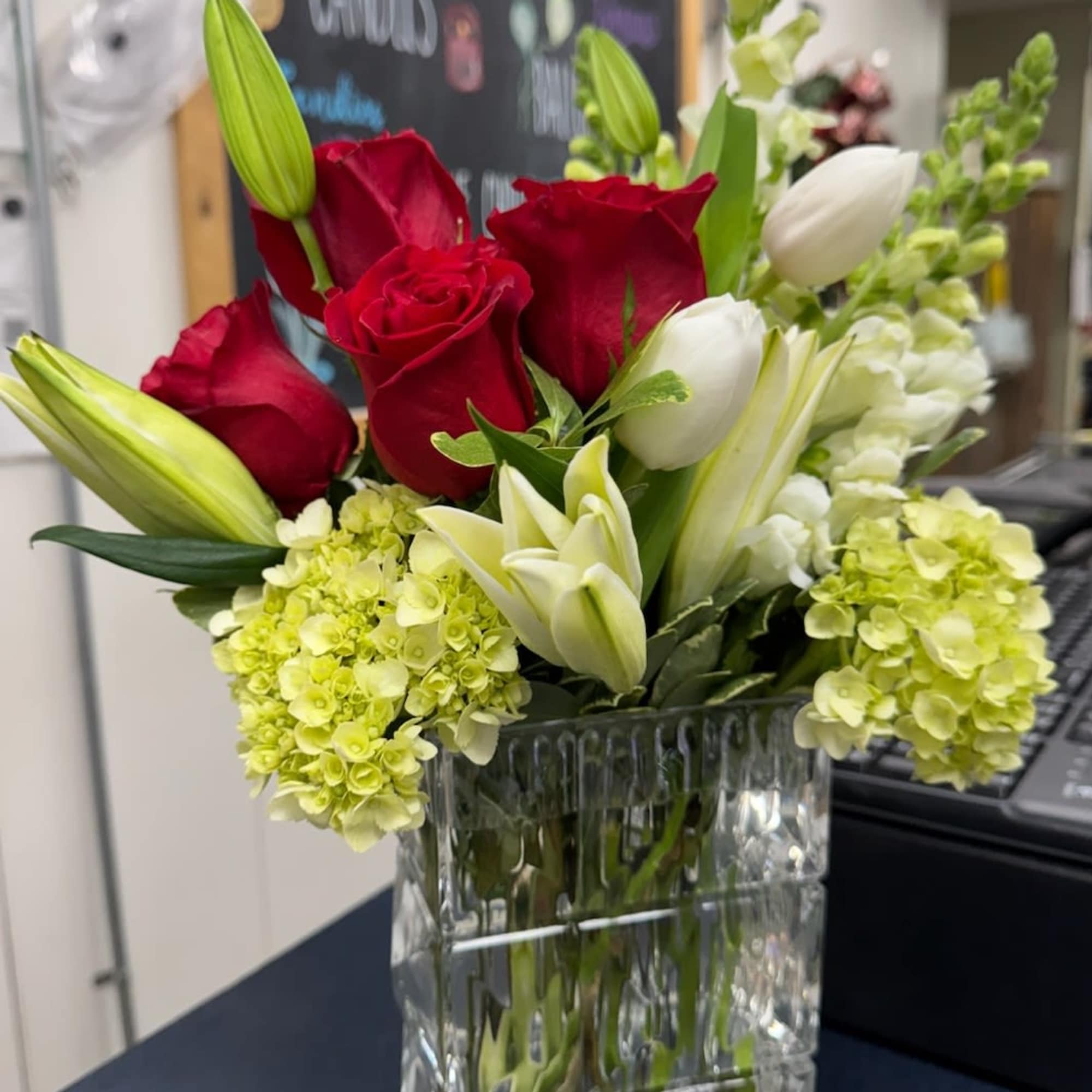 Red roses and white lilies in a clear glass vase with pale green hydrangeas