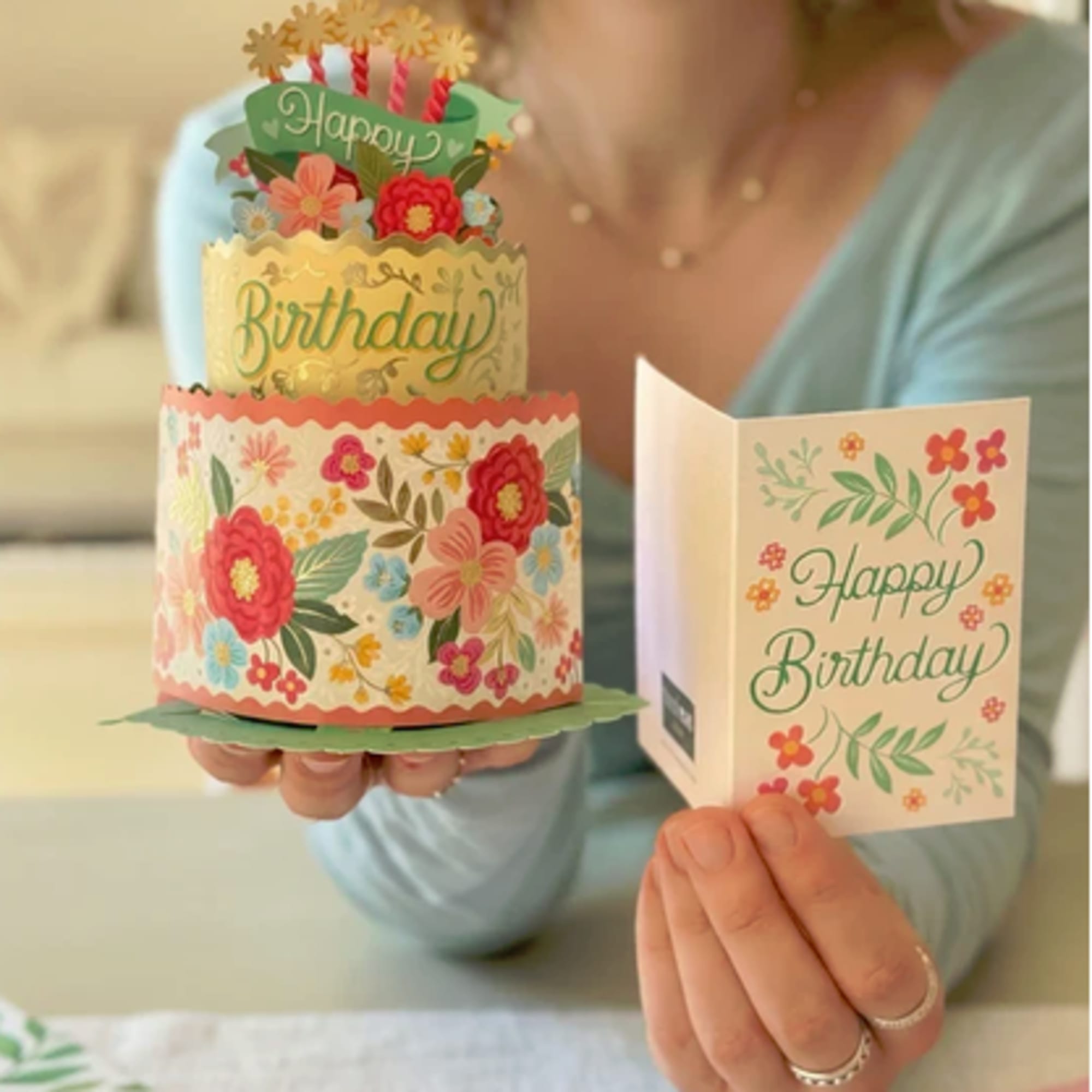 Woman holding a floral birthday card and a layered paper cake decoration
