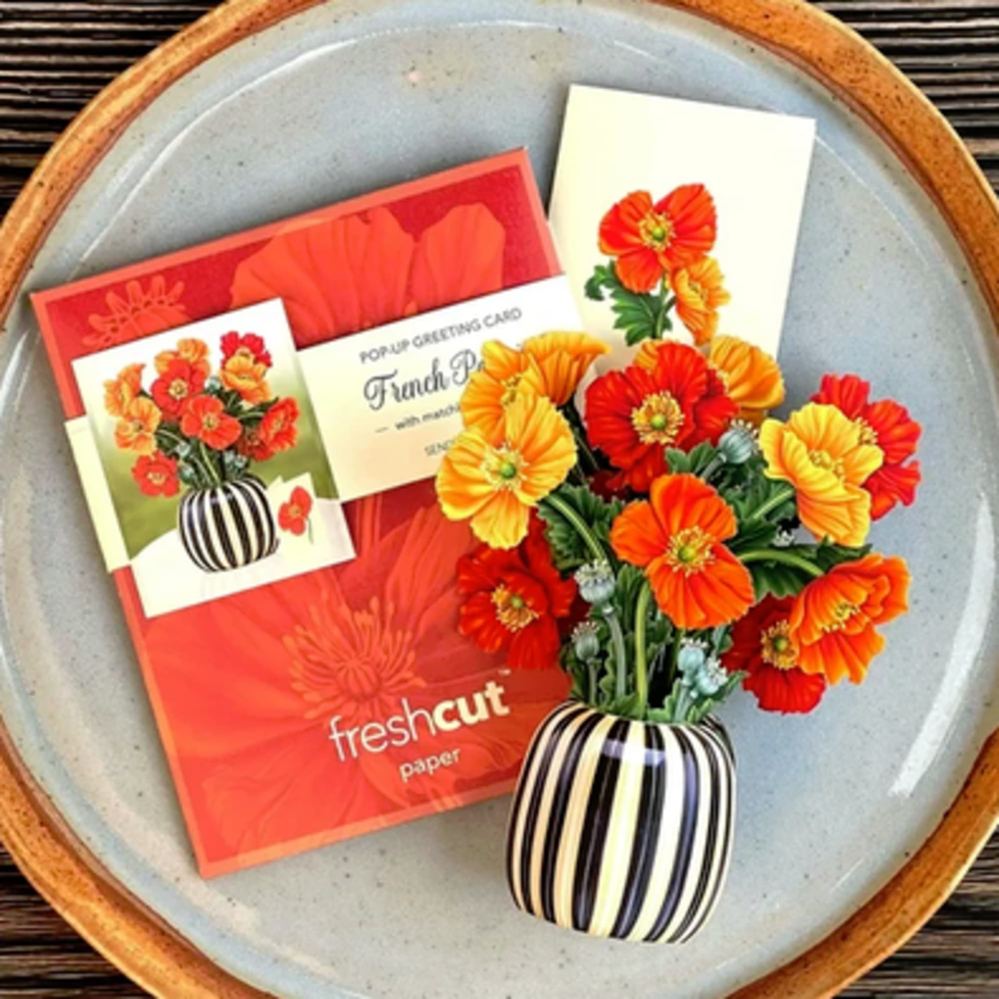 Bouquet of orange and yellow flowers in a striped vase with greeting cards