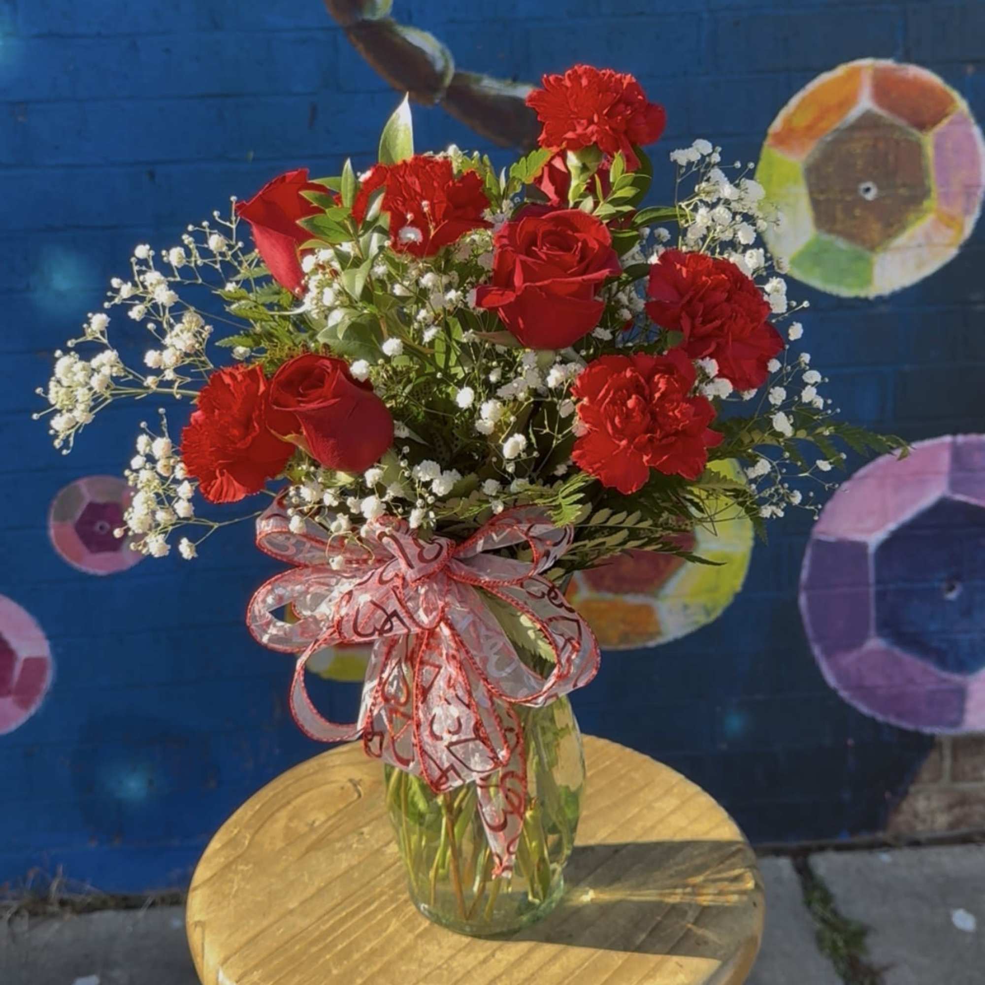 Red roses and carnations in a glass vase with a decorative ribbon