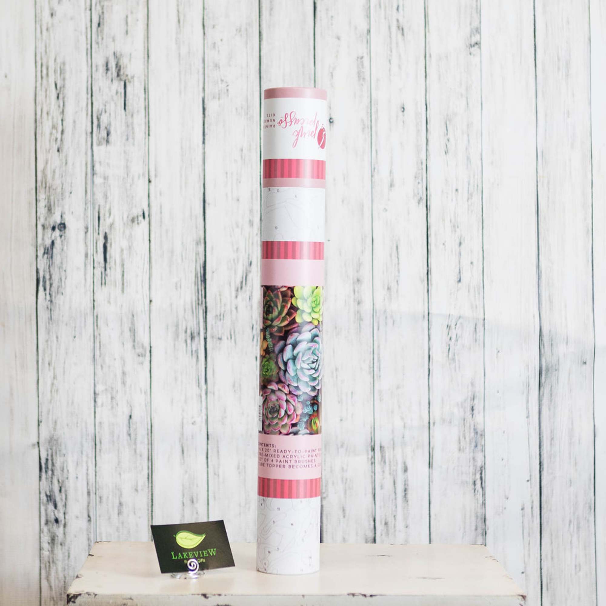 Tall cylindrical package with succulent artwork on a white wood background