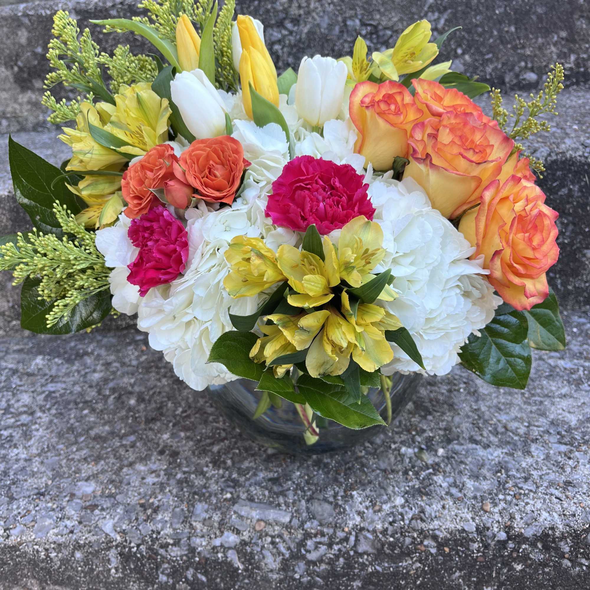 This arrangement has hydrangea, orange roses, yellow tulips, yellow alstroemeria, hot pink